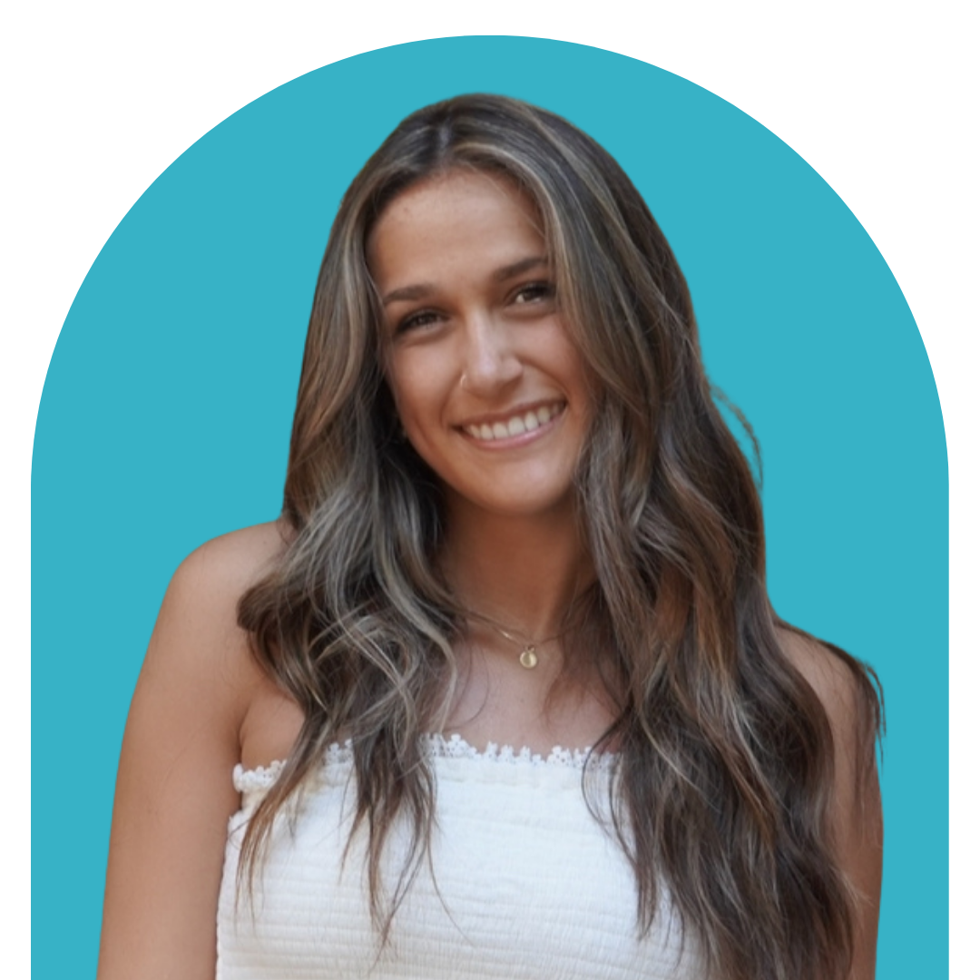 Smiling woman with long wavy hair wearing a white sleeveless top and a delicate necklace, posed against a blue background with an arched shape.