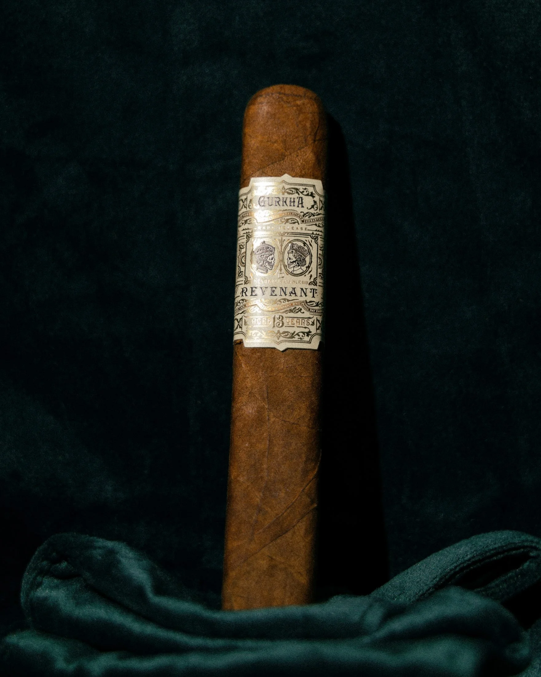 Hand-rolled cigar standing upright on dark green velvet, lit from the side in low warm light