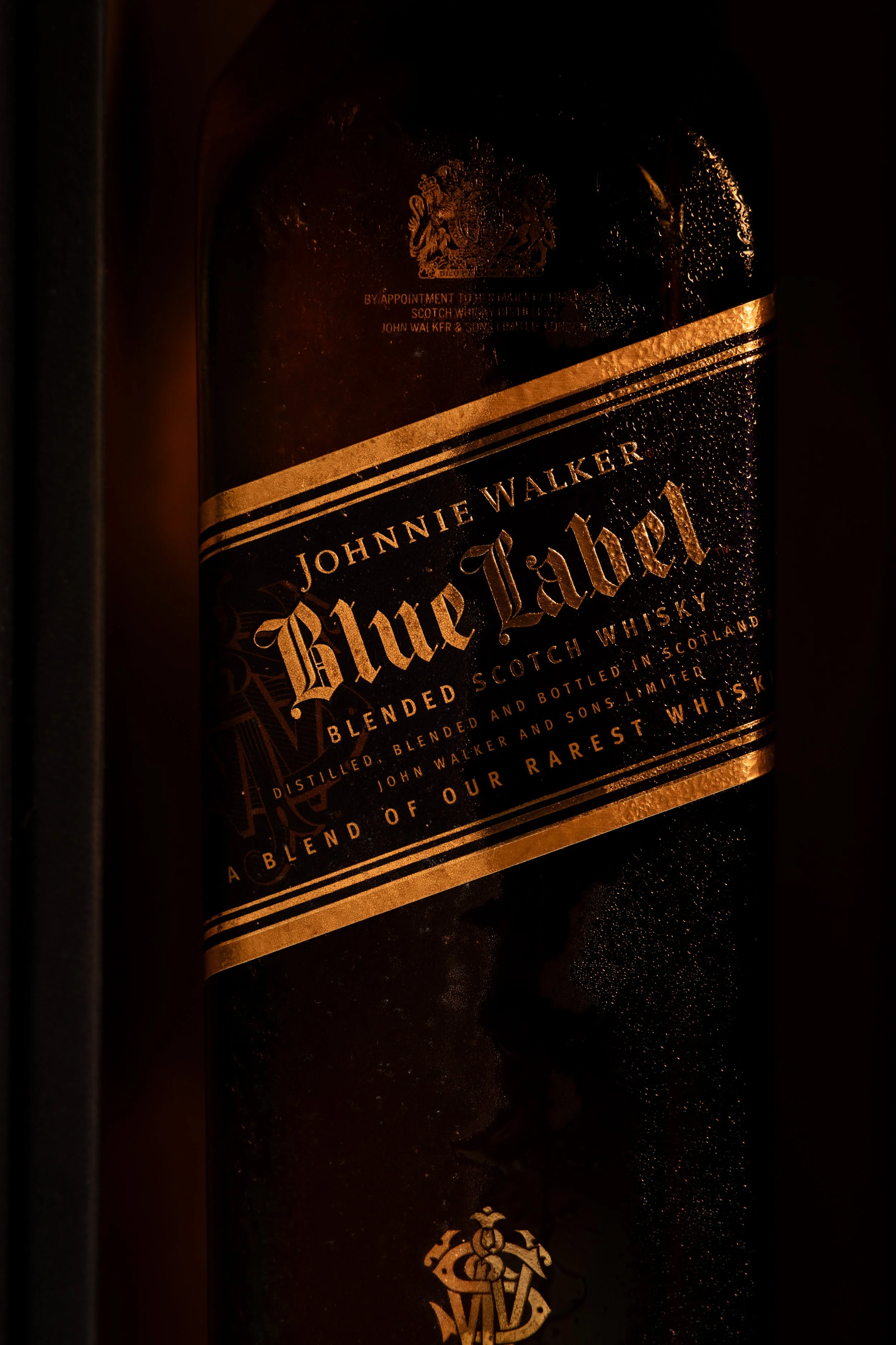 Close detail of an embossed gold whisky label raking into shadow, shot in low light