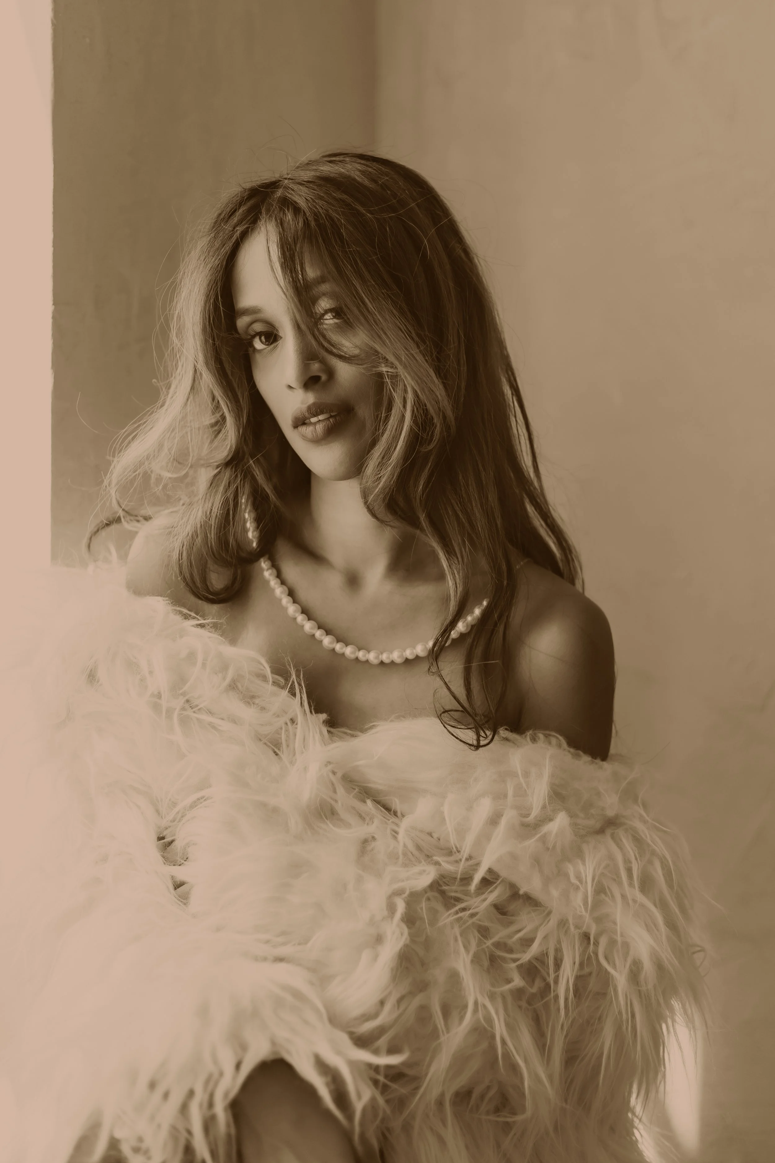 A woman with tousled hair wearing a pearl necklace, a fur coat, and glamorous makeup.