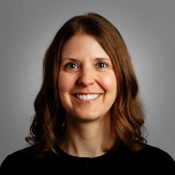 Kristy Kerr, a woman with shoulder-length brown hair smiling at the camera against a gray background.