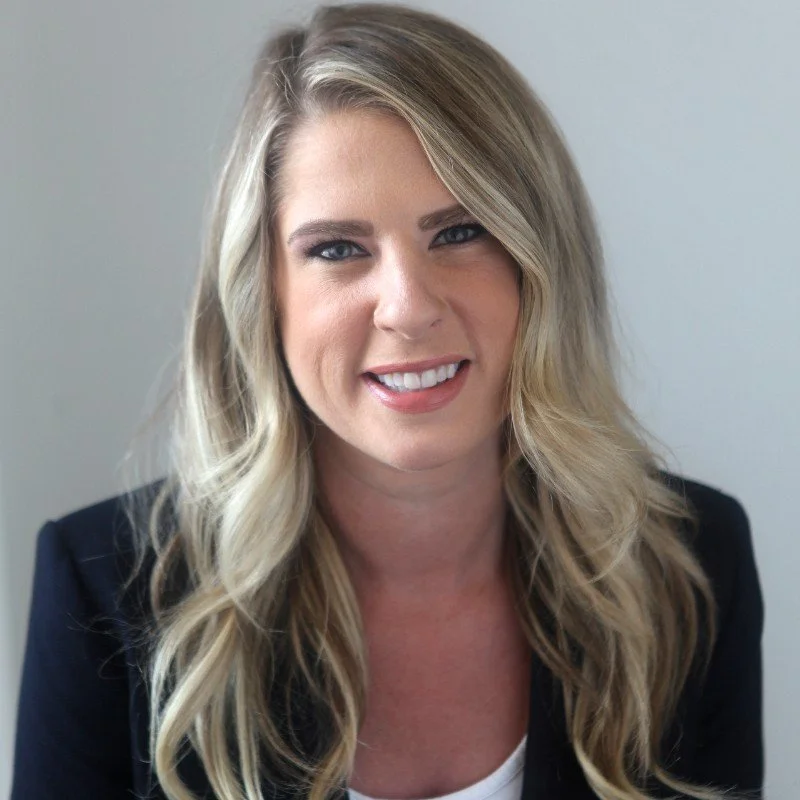 Brenda Ell, a smiling blonde woman with wavy hair wearing a black blazer and white top, posing against a light-colored background.