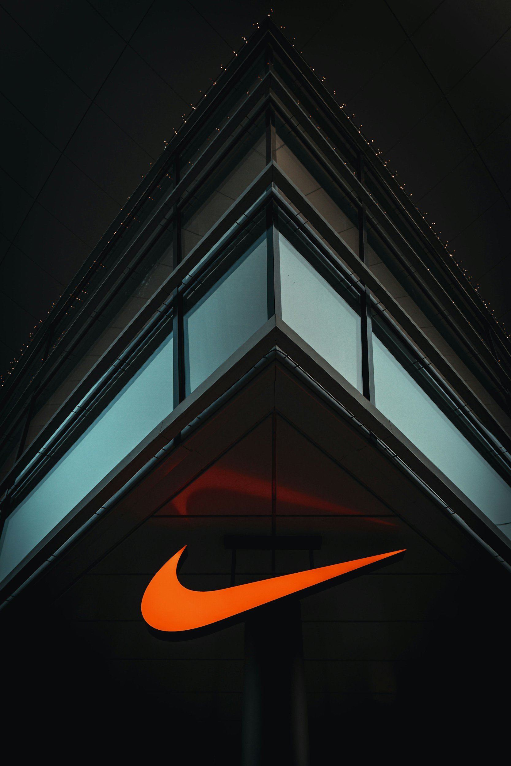 A modern building at night with illuminated windows and an orange Nike logo sign at the bottom.