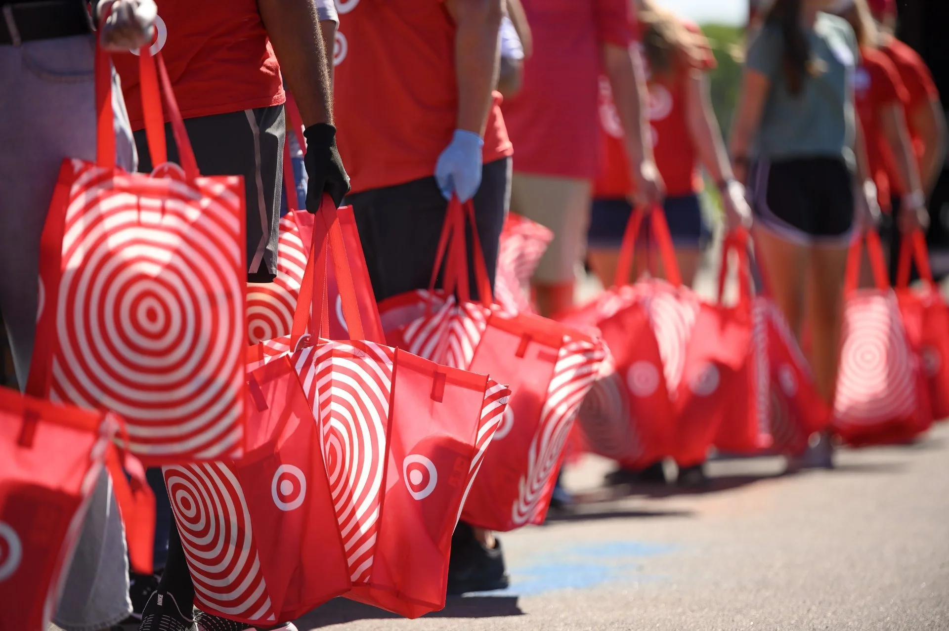 People standing in a line holding red shopping bags with Target store's logo, some wearing gloves and casual clothing.