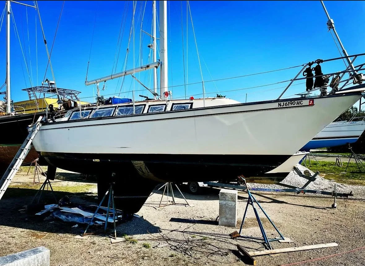 A white sailboat on land, supported by metal stands in the boat yard getting a Powerflow Marine motor installed