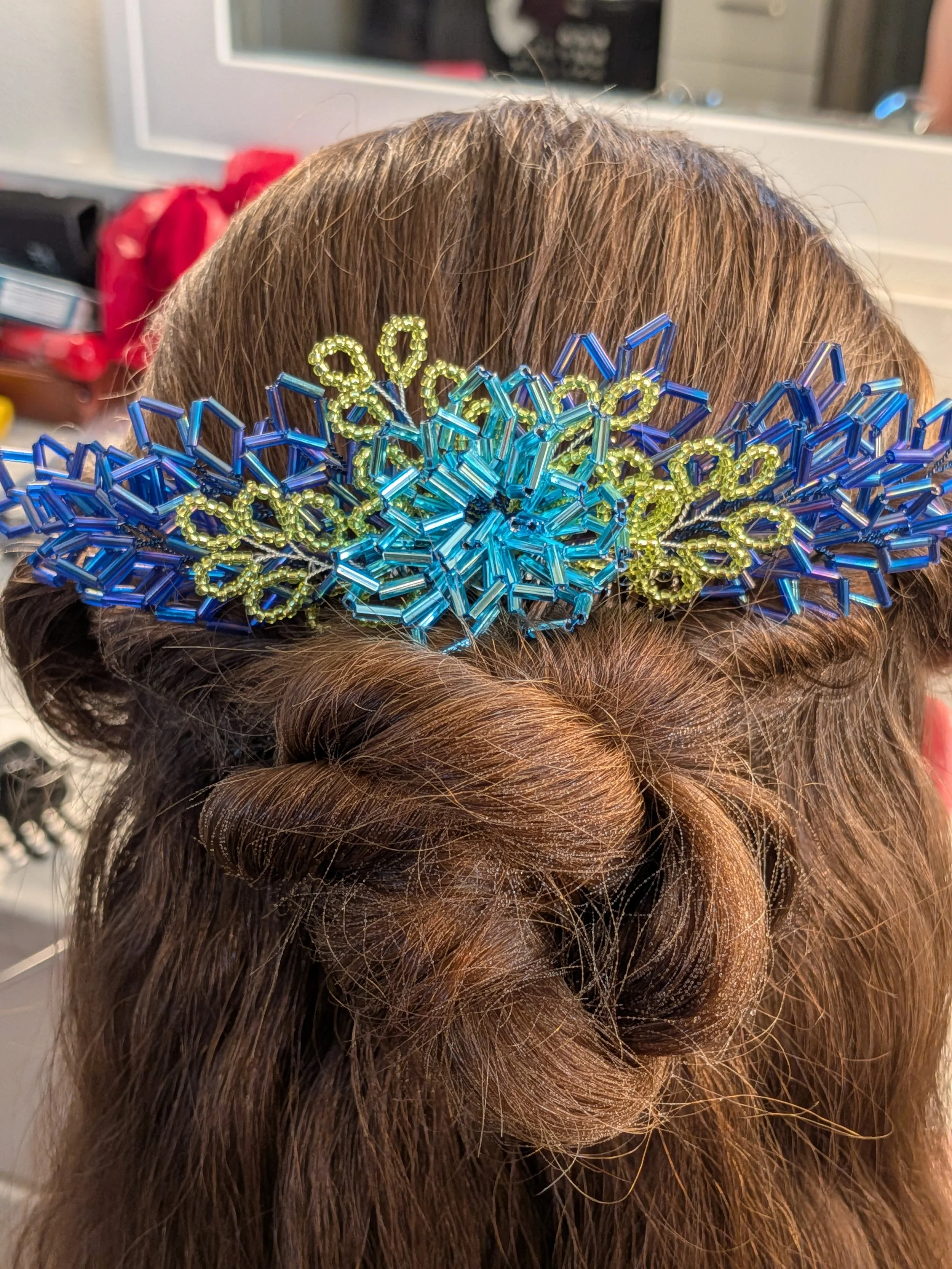 Brown hair styled in a rolled braid with a colorful beaded haircomb featuring blue and yellow beads, placed on top of the hair.