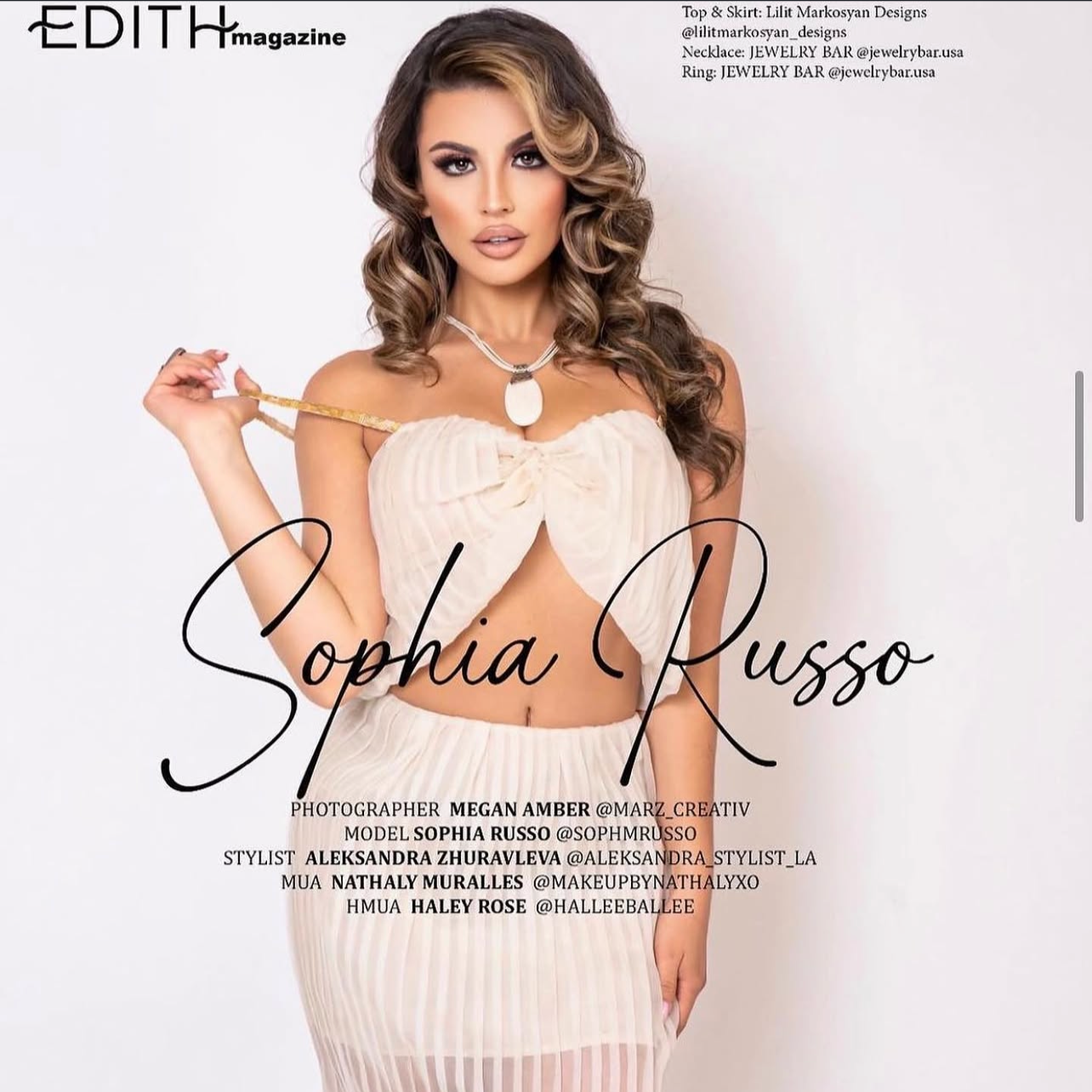 Magazine cover featuring model Sophia Russo in a cream-colored, pleated, off-shoulder top and matching skirt. She has long, wavy brown hair and makeup with bold eye makeup. She holds one strap of her top in her right hand. The cover includes text with her name, photographer, stylist, makeup artist, and stylist social media handles.