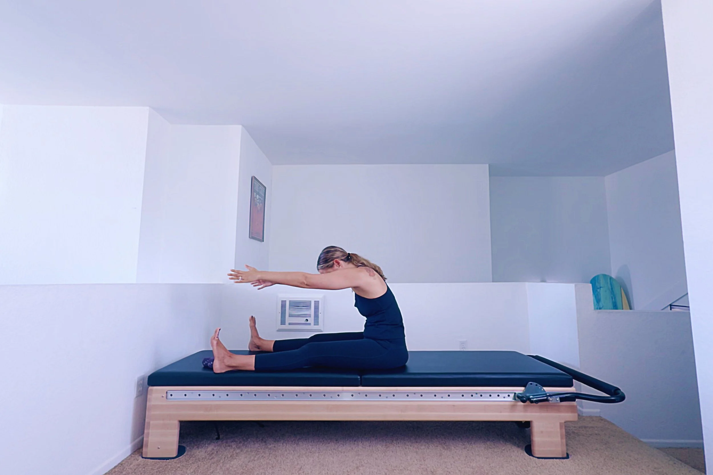 Pilates instructor demonstrating Spine Stretch Forward exercise for spinal health and posture improvement.