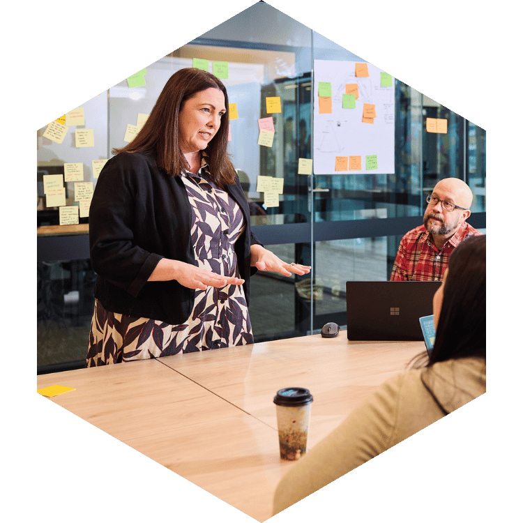 Businesswoman speaking to colleagues in a meeting room with sticky notes on the glass wall.