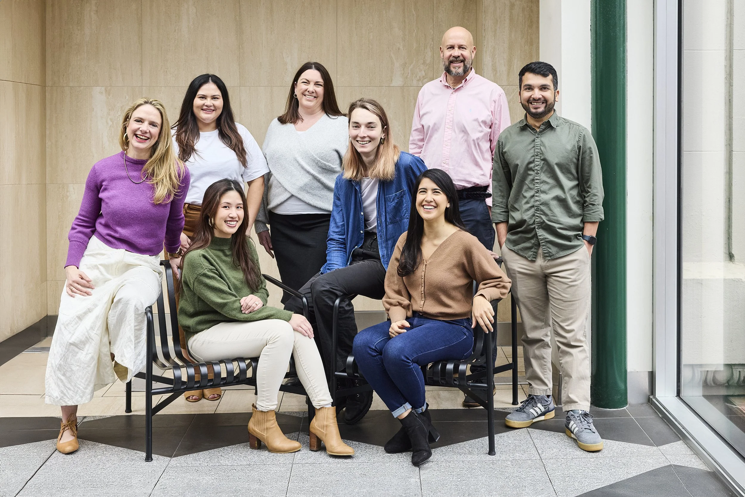 Group of nine diverse people smiling and posing together indoors near a large window.
