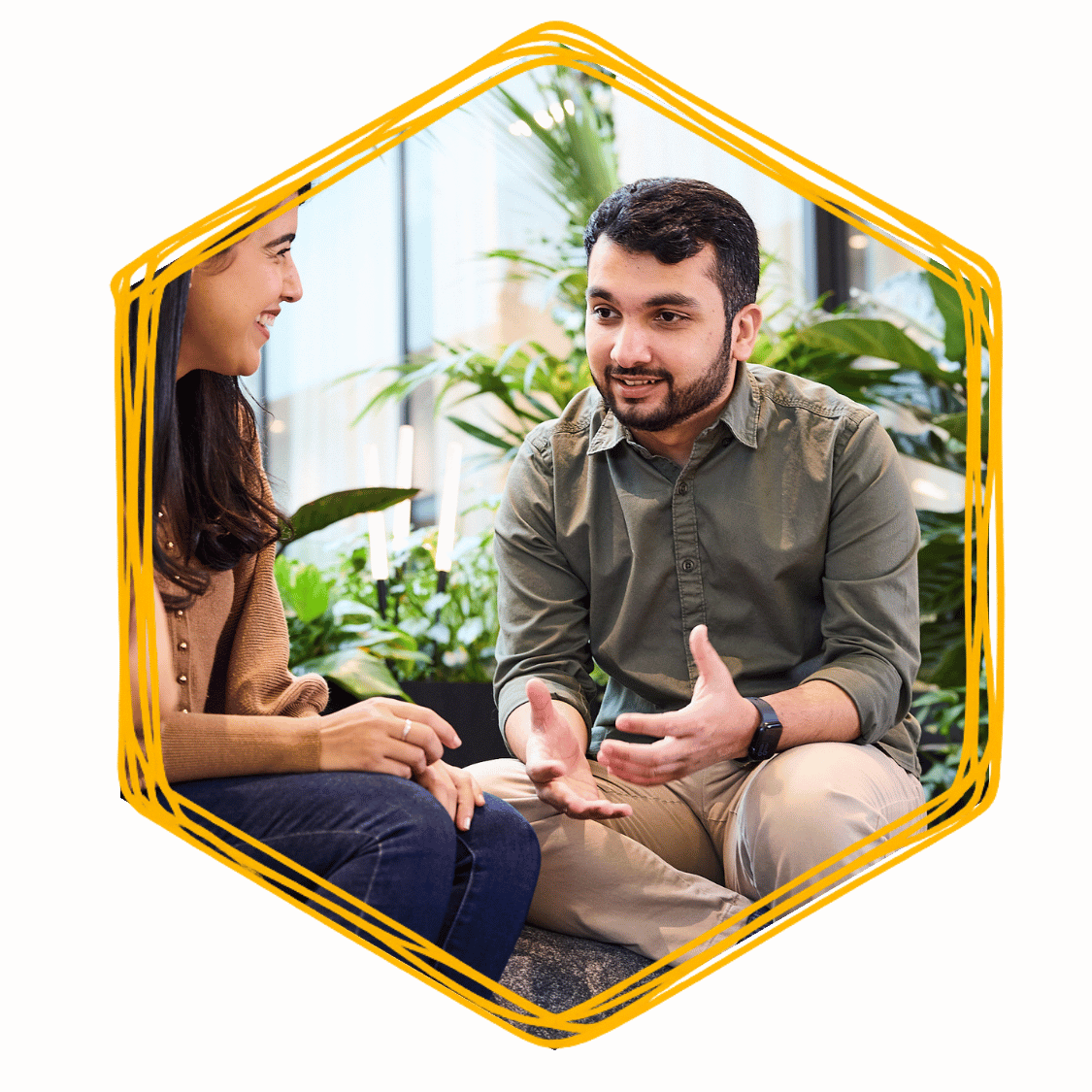 A man and woman having a conversation in a bright, green indoor space with plants in the background.