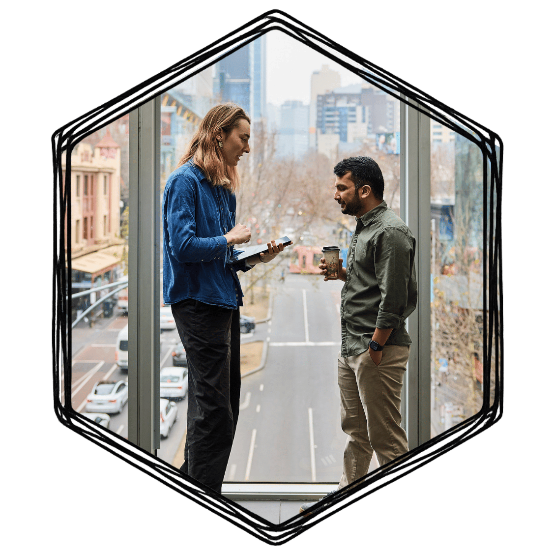 A woman and a man stand in a window frame with a city street view in the background. The woman is holding a notepad and a pen, and the man is holding a coffee cup. They are engaged in conversation.
