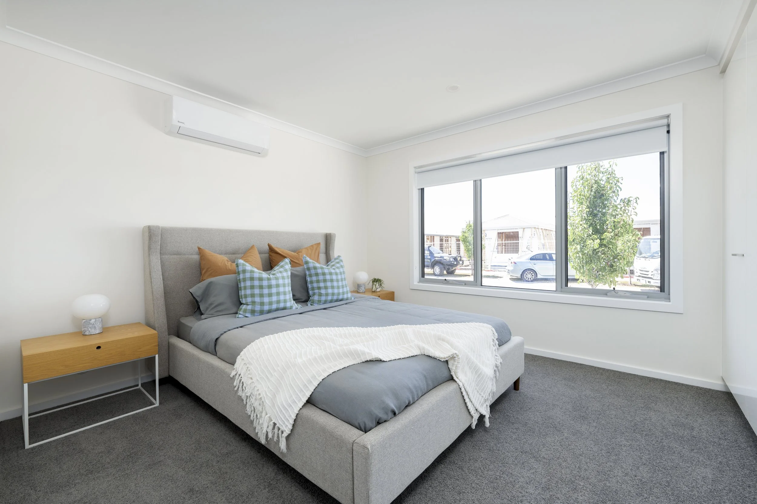 Bright main bedroom with large window, cosy bedding and soft carpet in an over 50s community home.