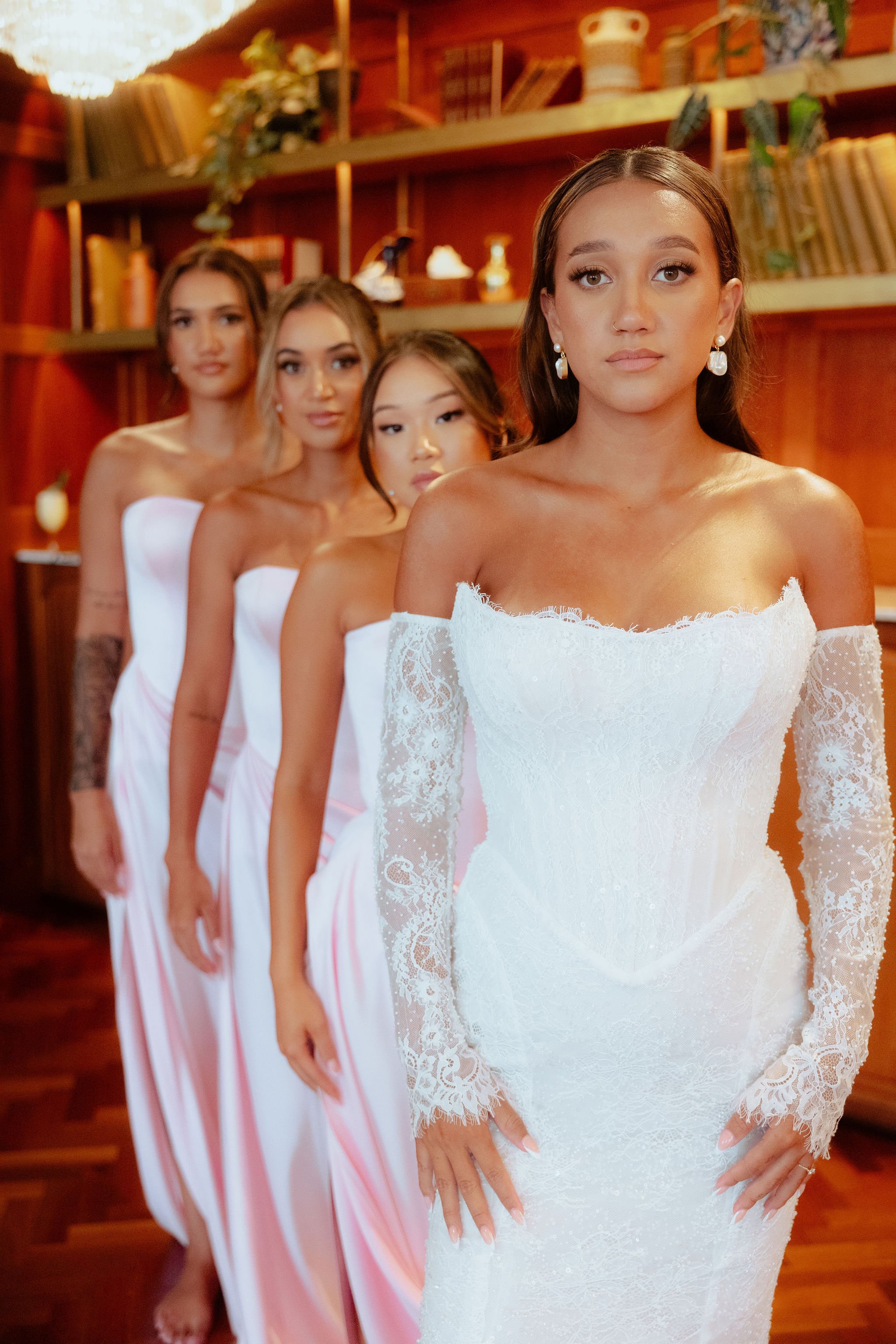 A man in a black tuxedo with a bow tie stands behind a woman in a white strapless gown outside a building with stone walls and steps.