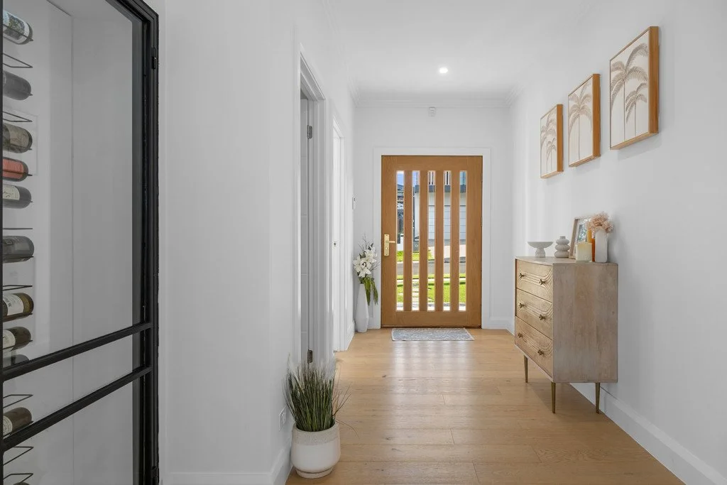 Entryway with wooden front door, white walls, hardwood floor, decorative artwork, sideboard with vases and decor, potted plants, and a wine rack.