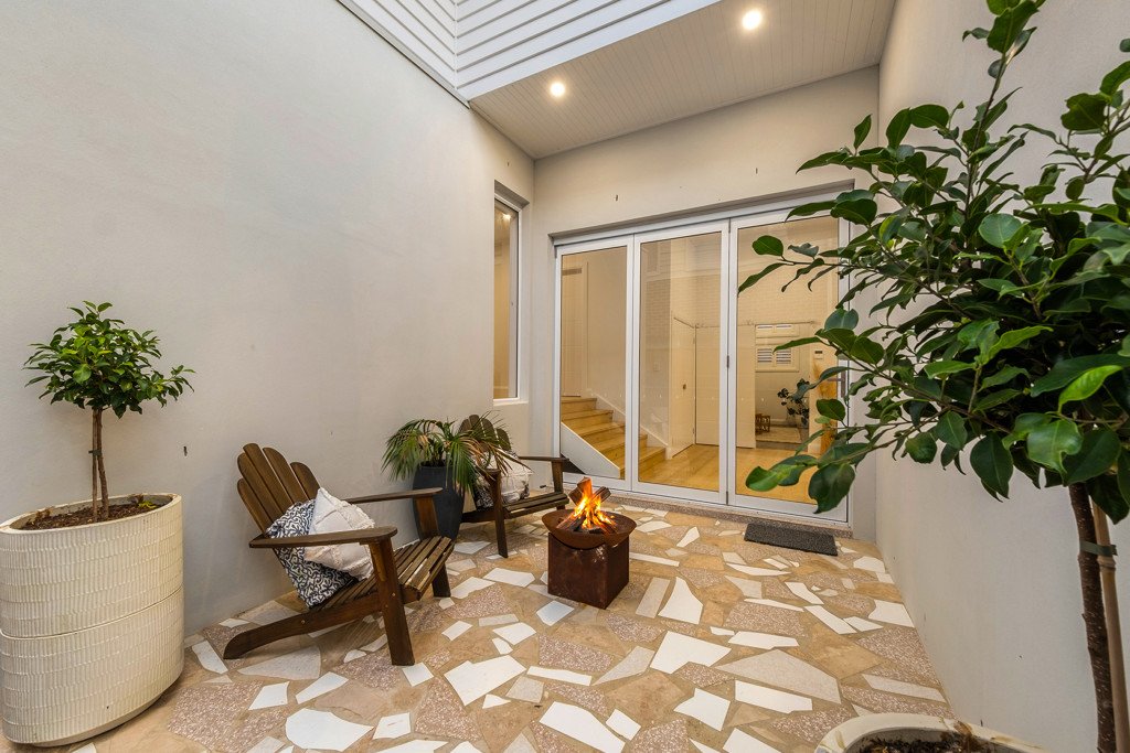 Indoor patio with two potted plants, wooden benches, a fire pit, and a large glass sliding door leading inside a house.