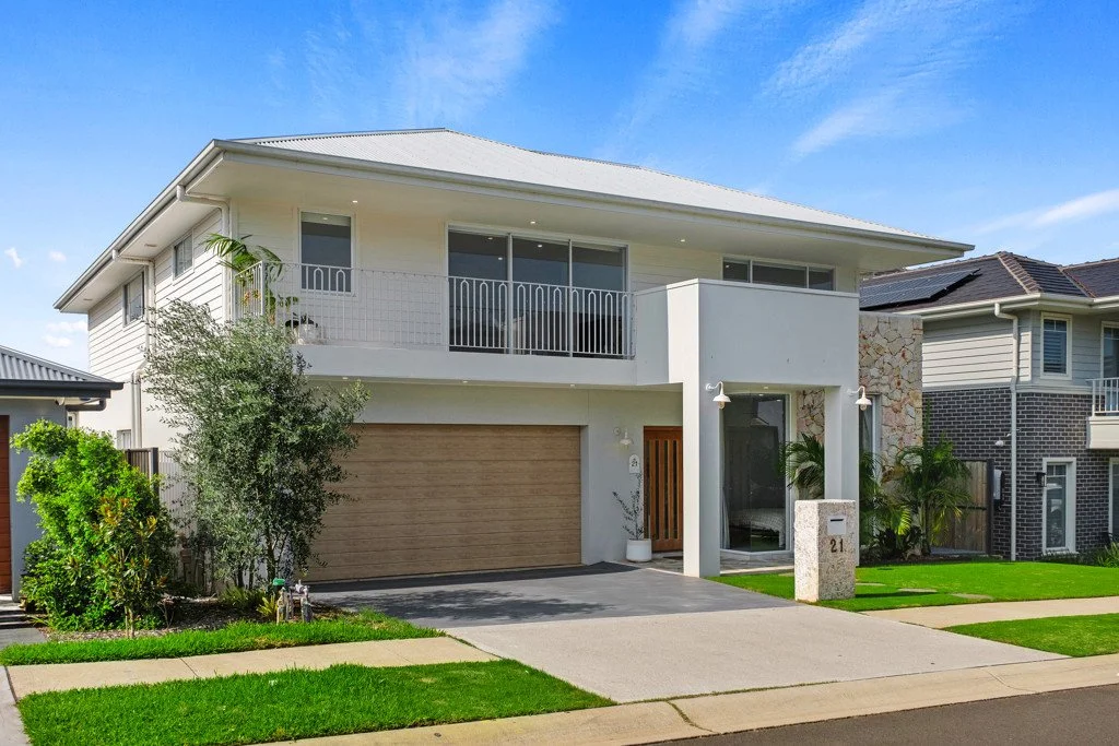 Modern two-story house with white exterior, wooden garage door, and a small front yard with green grass and plants.
