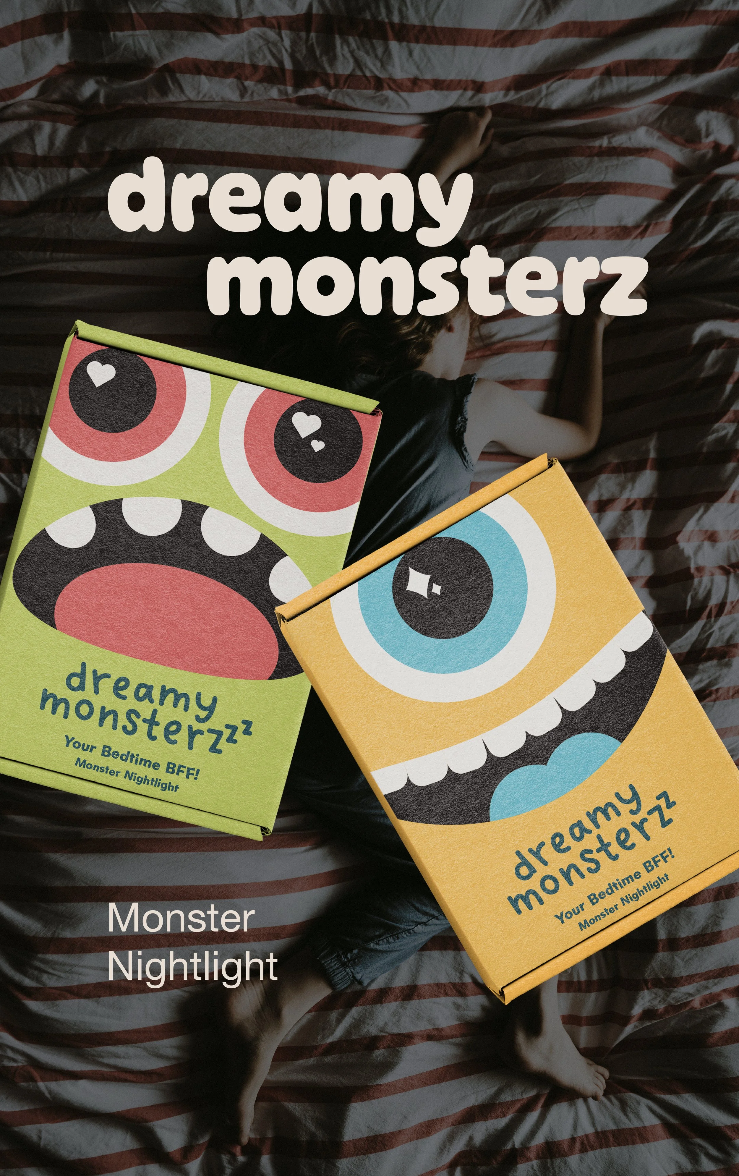 Two colorful boxes with cartoon monster faces labeled 'dreamy monsterz' resting on a bed with a child sleeping underneath a striped blanket.