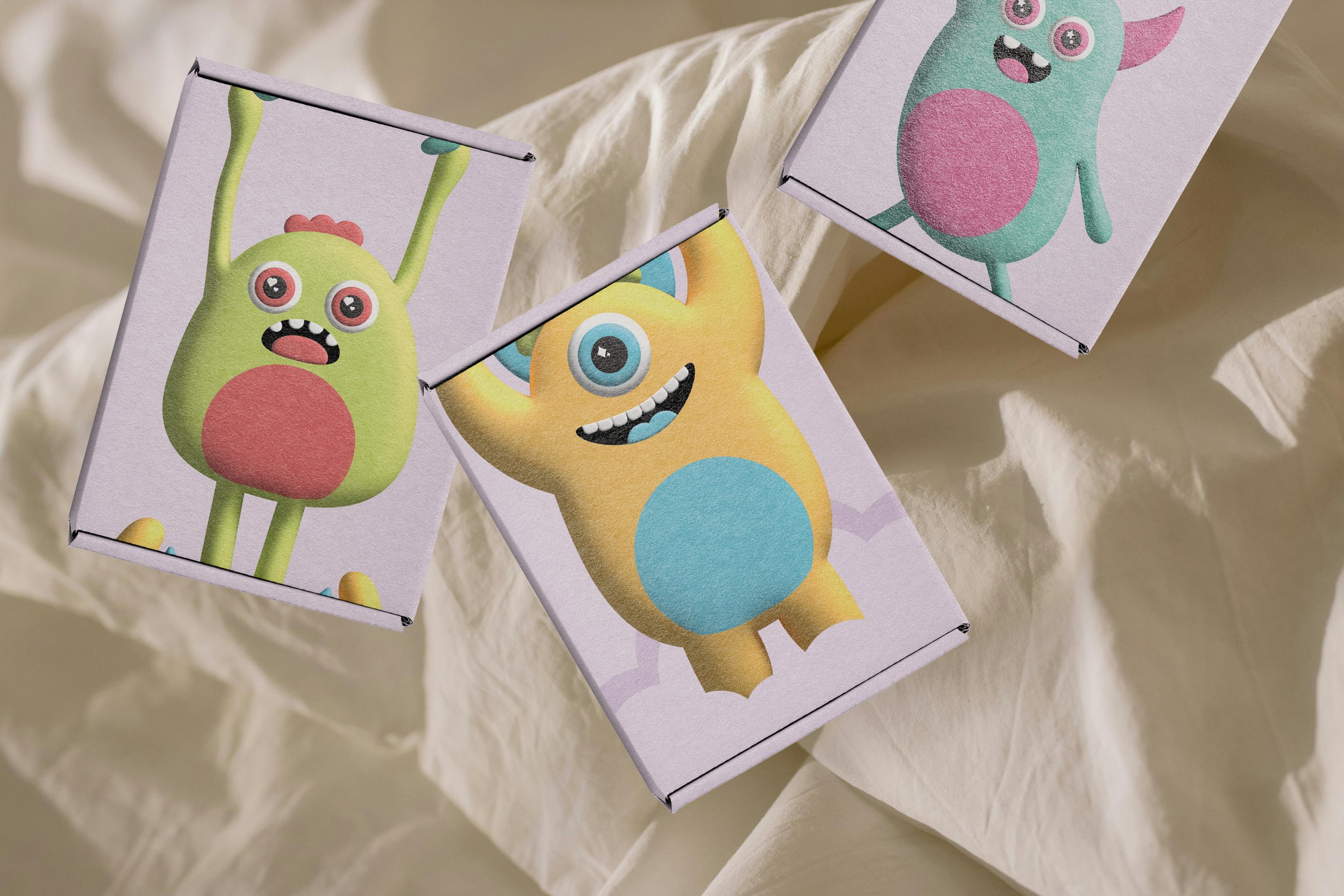 Colorful cardboard boxes with cartoon monster and creature illustrations on a beige fabric surface.