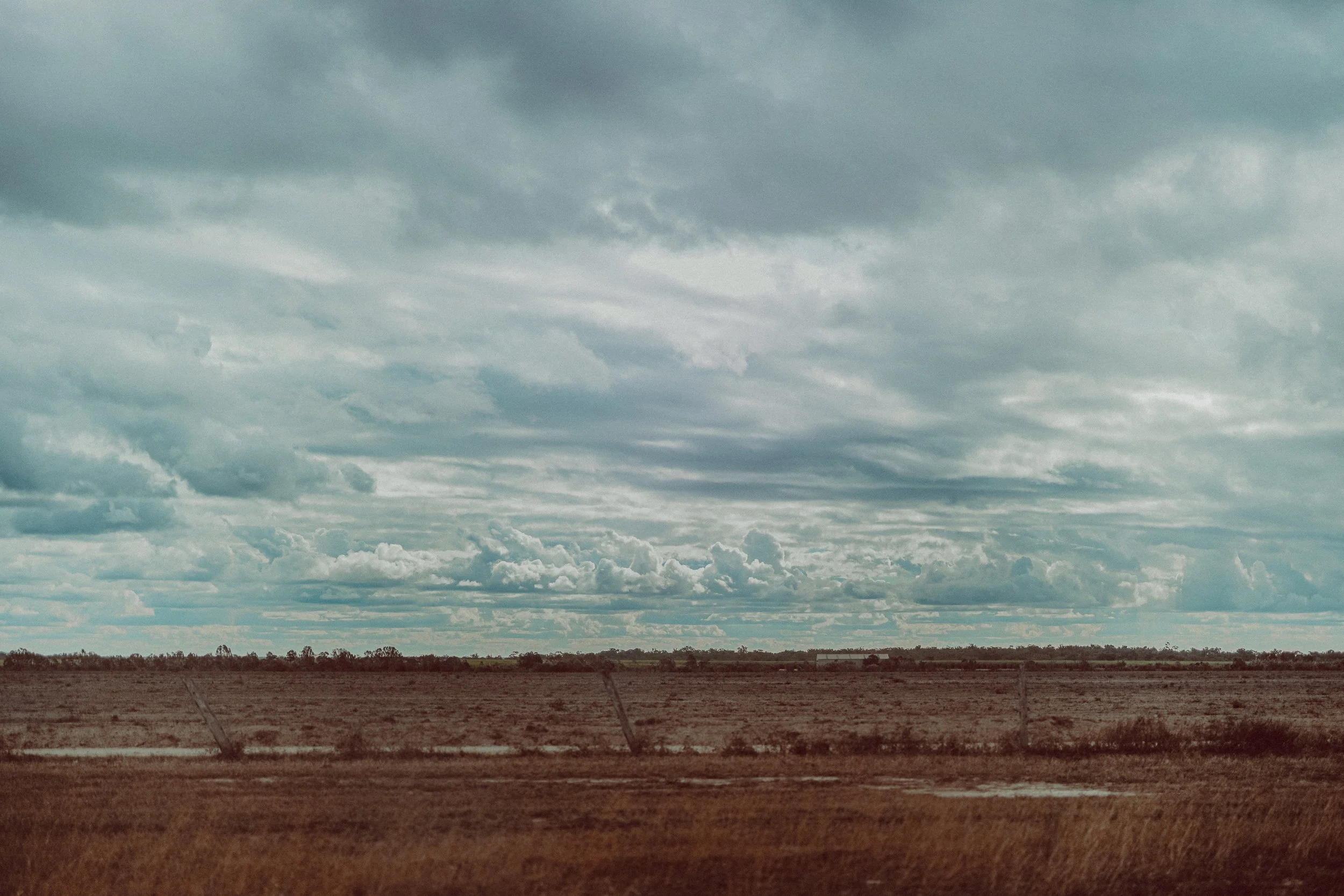 Wide view of a flat, dry landscape with brown grass and a barbed wire fence, under a cloudy sky