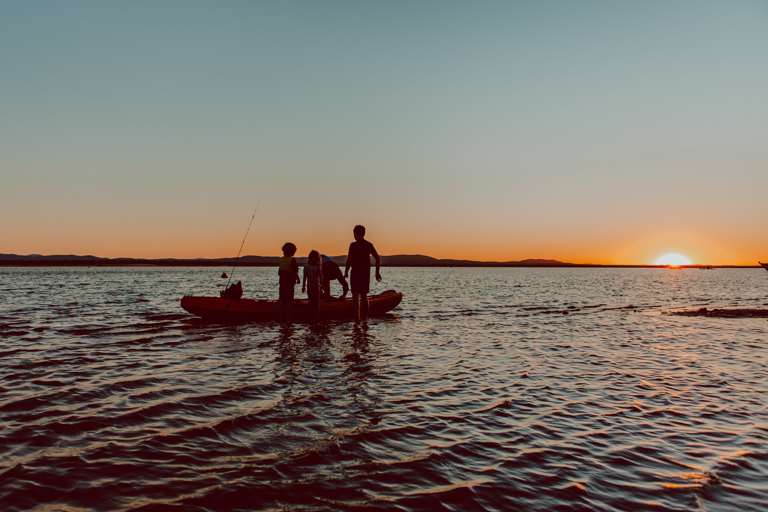 Silhouettes of four people on a boat during sunset on a body of water.