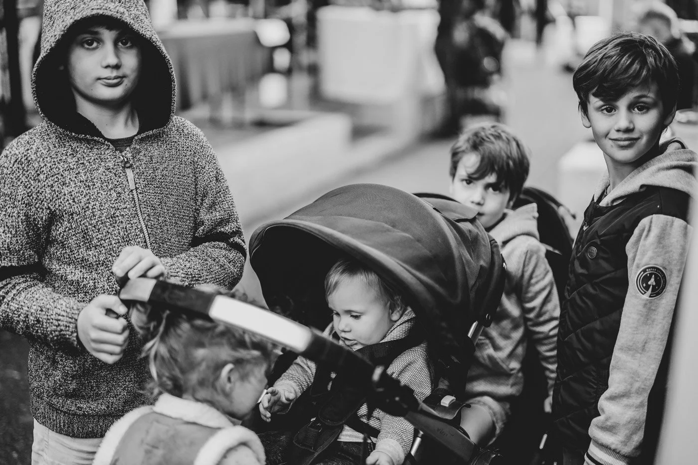 Children waiting in line outdoors, some with a stroller, in a black and white photo.