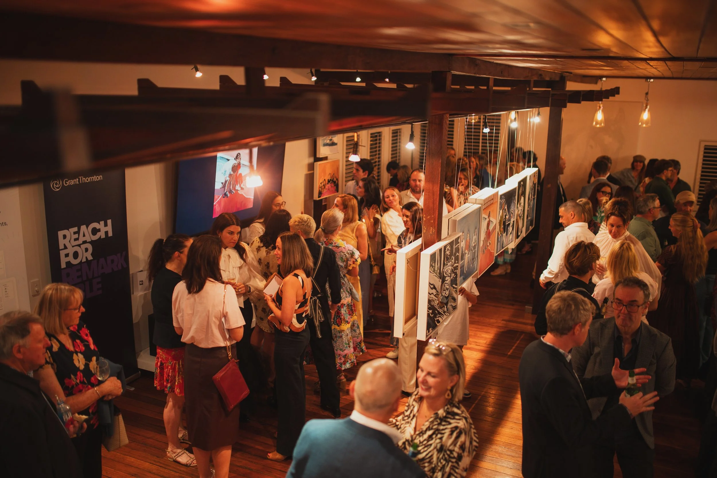 A group of friends smiling and celebrating with drinks outside on a patio or terrace in a sunny setting.