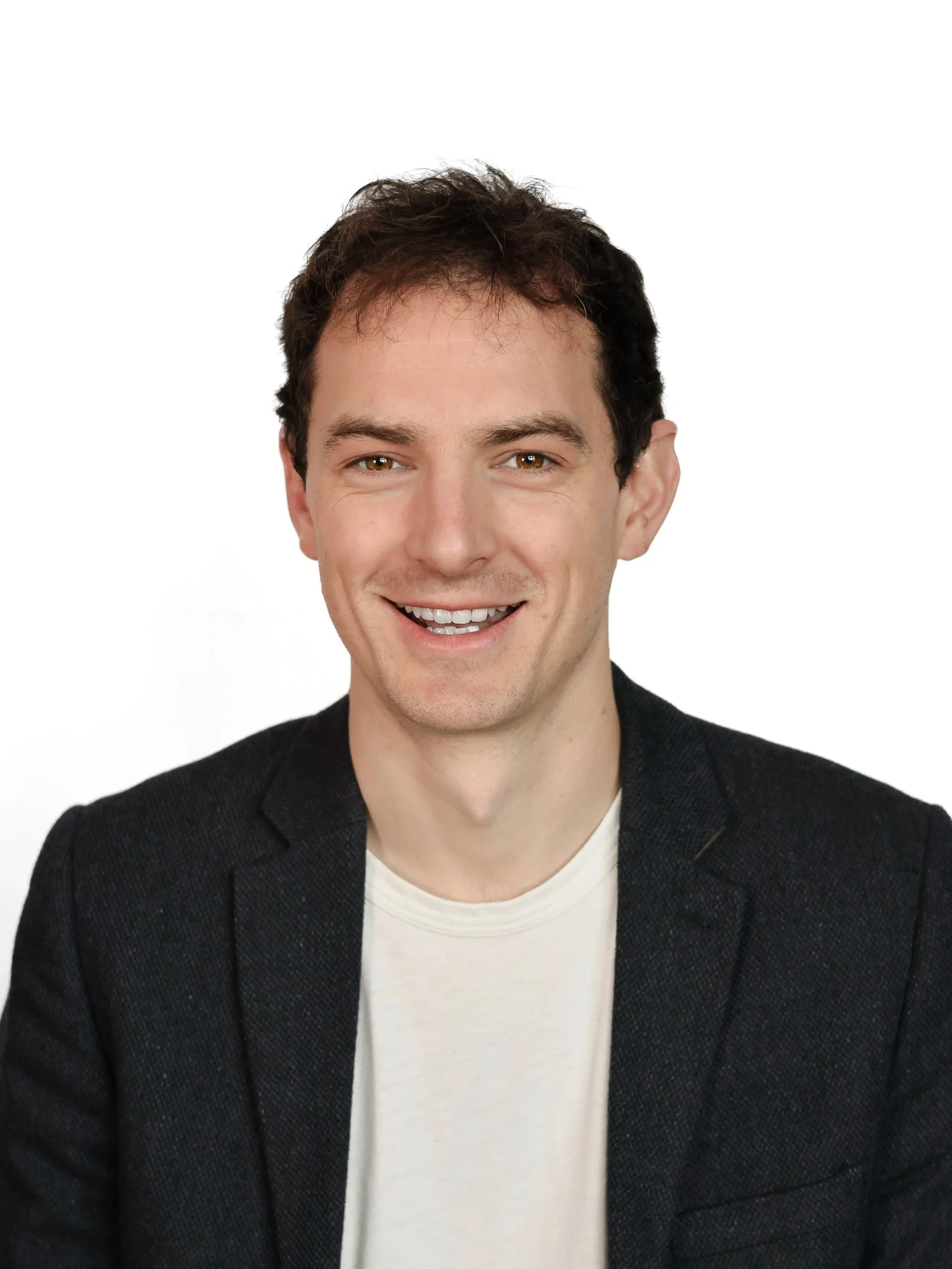 Smiling young man in a black blazer and white shirt against a white background.