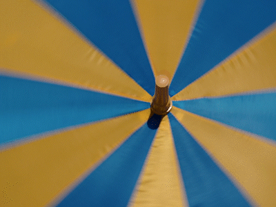 Close-up of a beach umbrella with blue and yellow panels and a wooden pole.