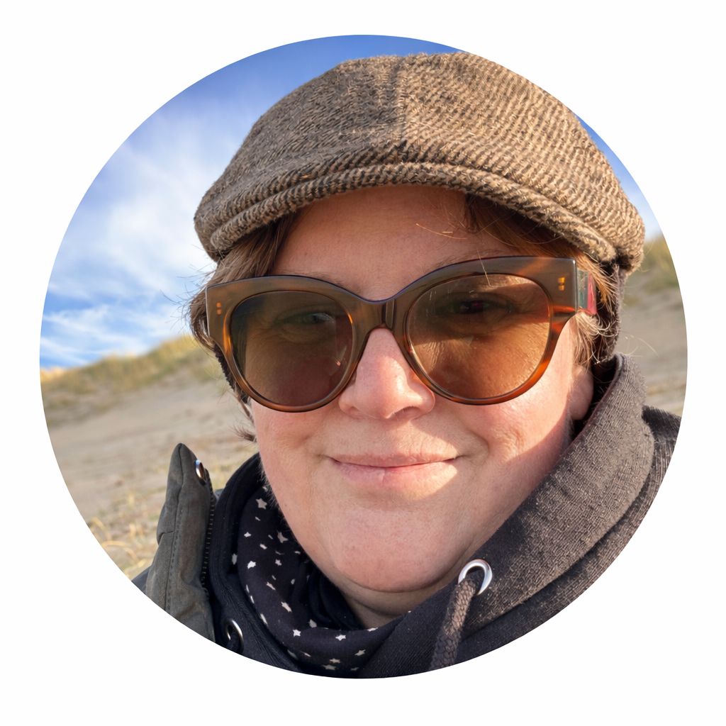 Een persoon met een pet en grote zonnebril maakt een selfie op het strand bij zonsondergang.