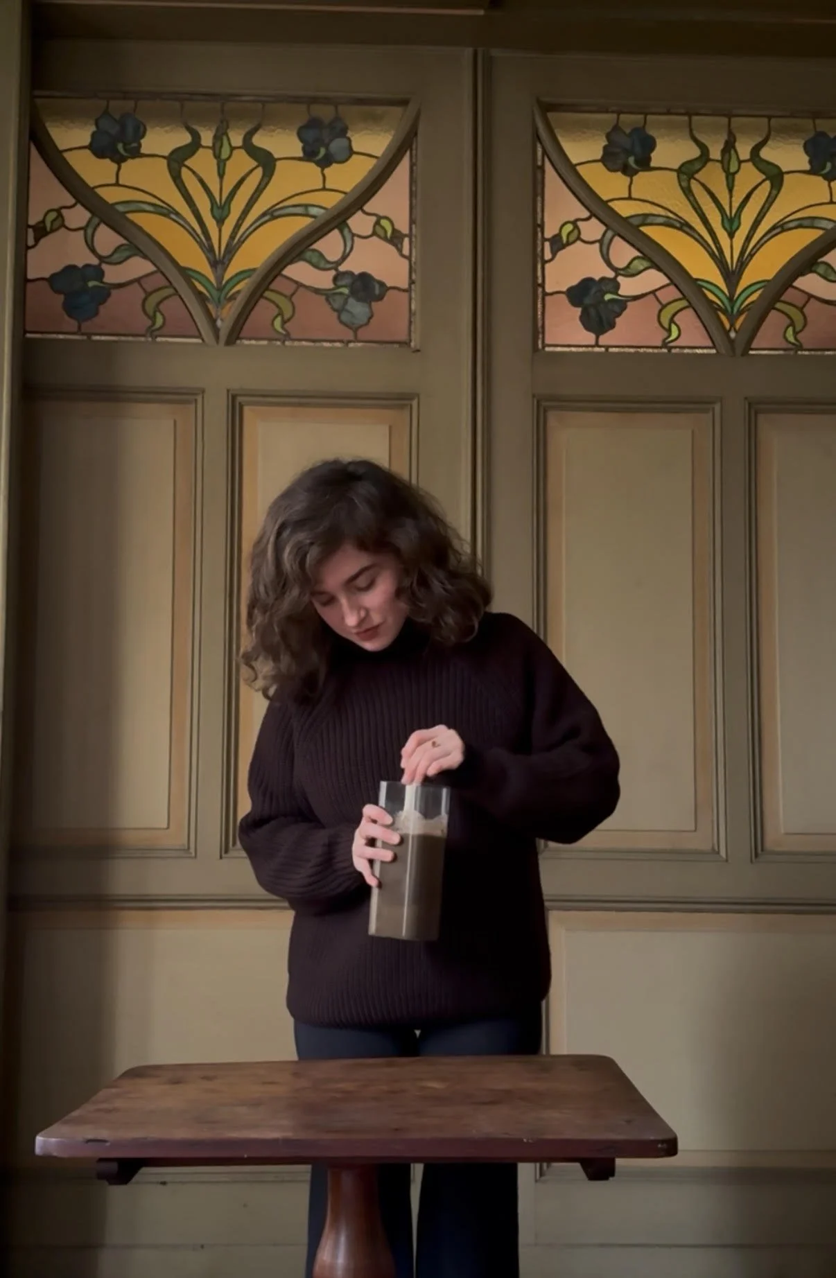 Ecologisch hovenier en tuinontwerper die een glazen pot een bodemtest doet, in een orangerie met decoratieve houten deur met stained glass ramen.