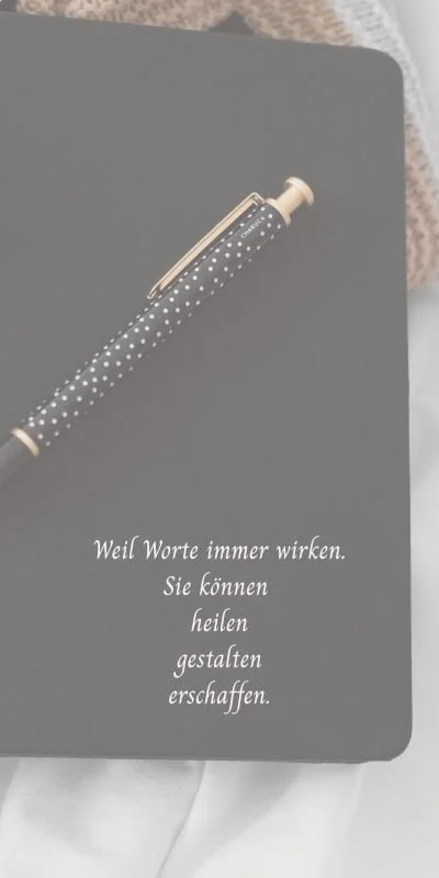 Schwarzes Notizbuch mit einem gepunkteten Stift darauf. Der Text auf dem Notizbuch lautet: "Weil Worte immer wirken. Sie können heilen, gestalten, erschaffen."