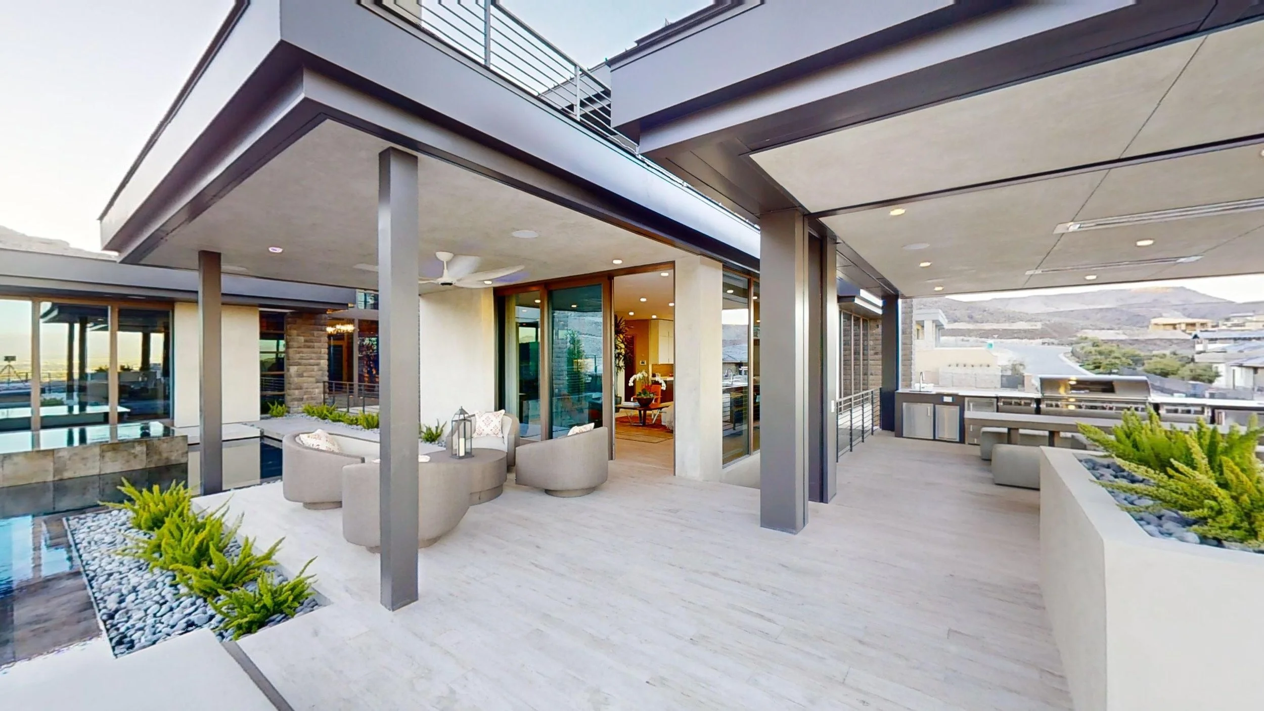 Modern rooftop balcony with outdoor seating, planters with greenery, and city and hillside views in the background.