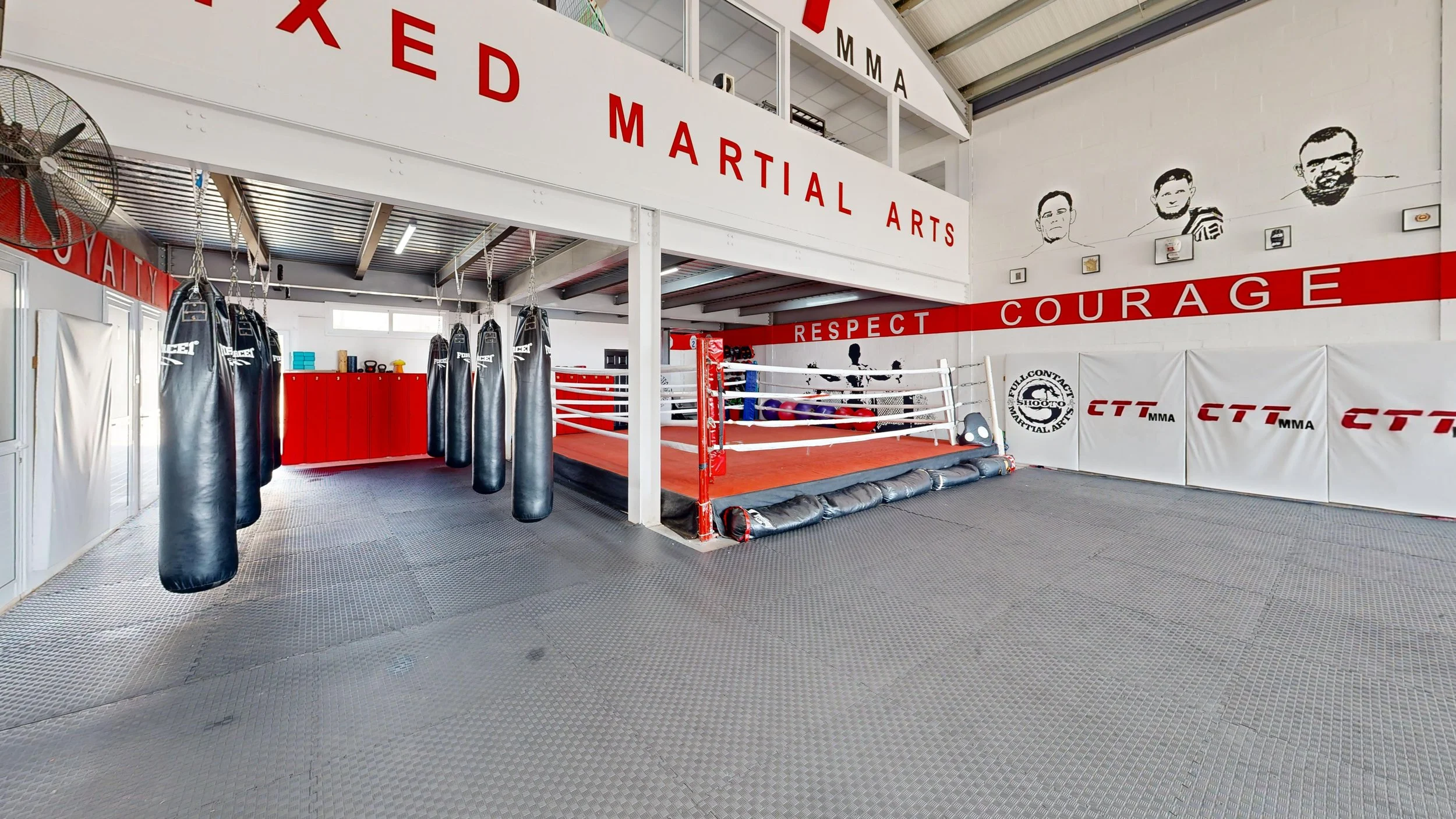 Empty martial arts gym with boxing rings, punching bags, and training equipment, with motivational words on the walls.