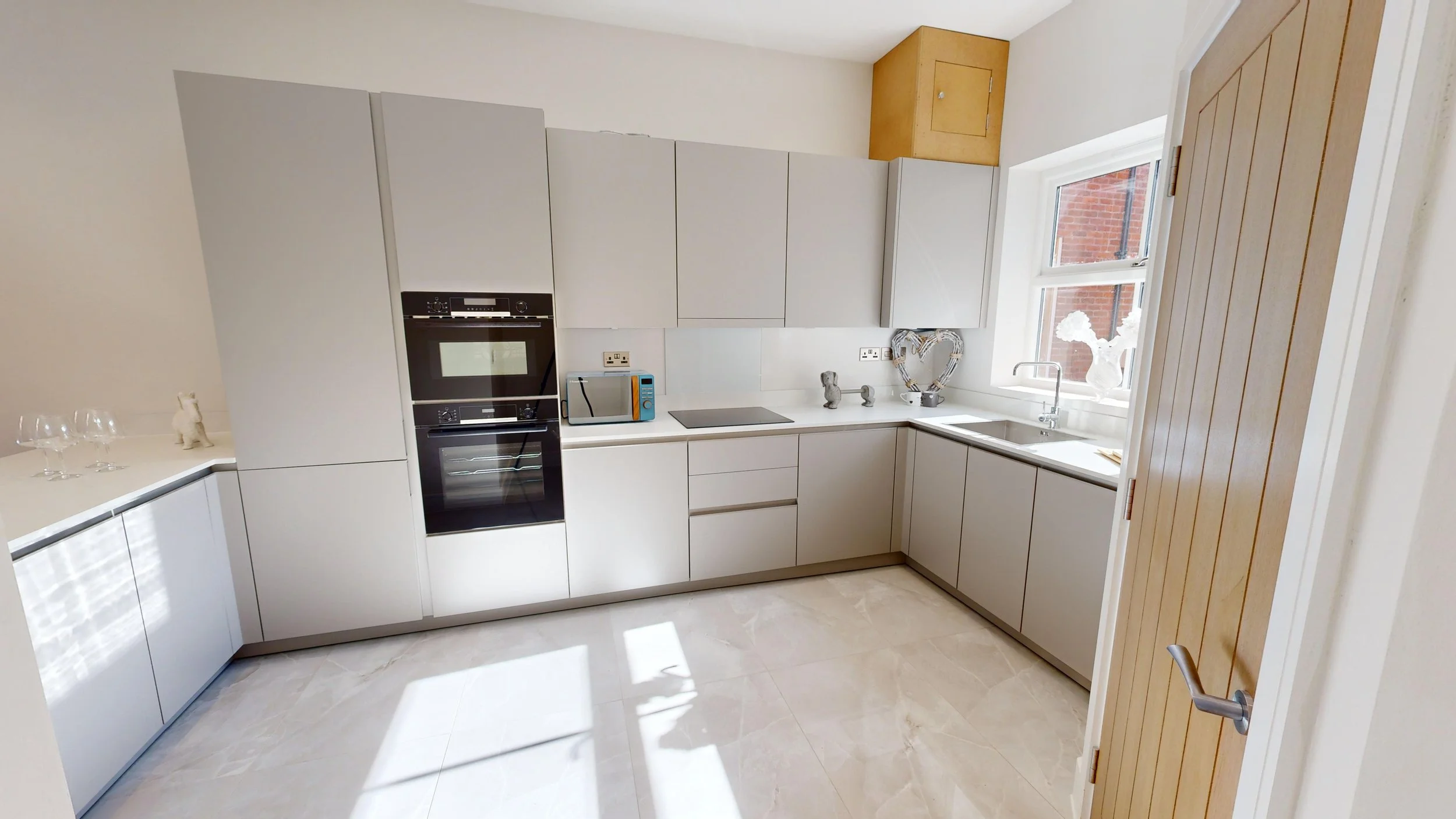 Modern kitchen with white cabinets, black oven, microwave, and a window with decorative vases.