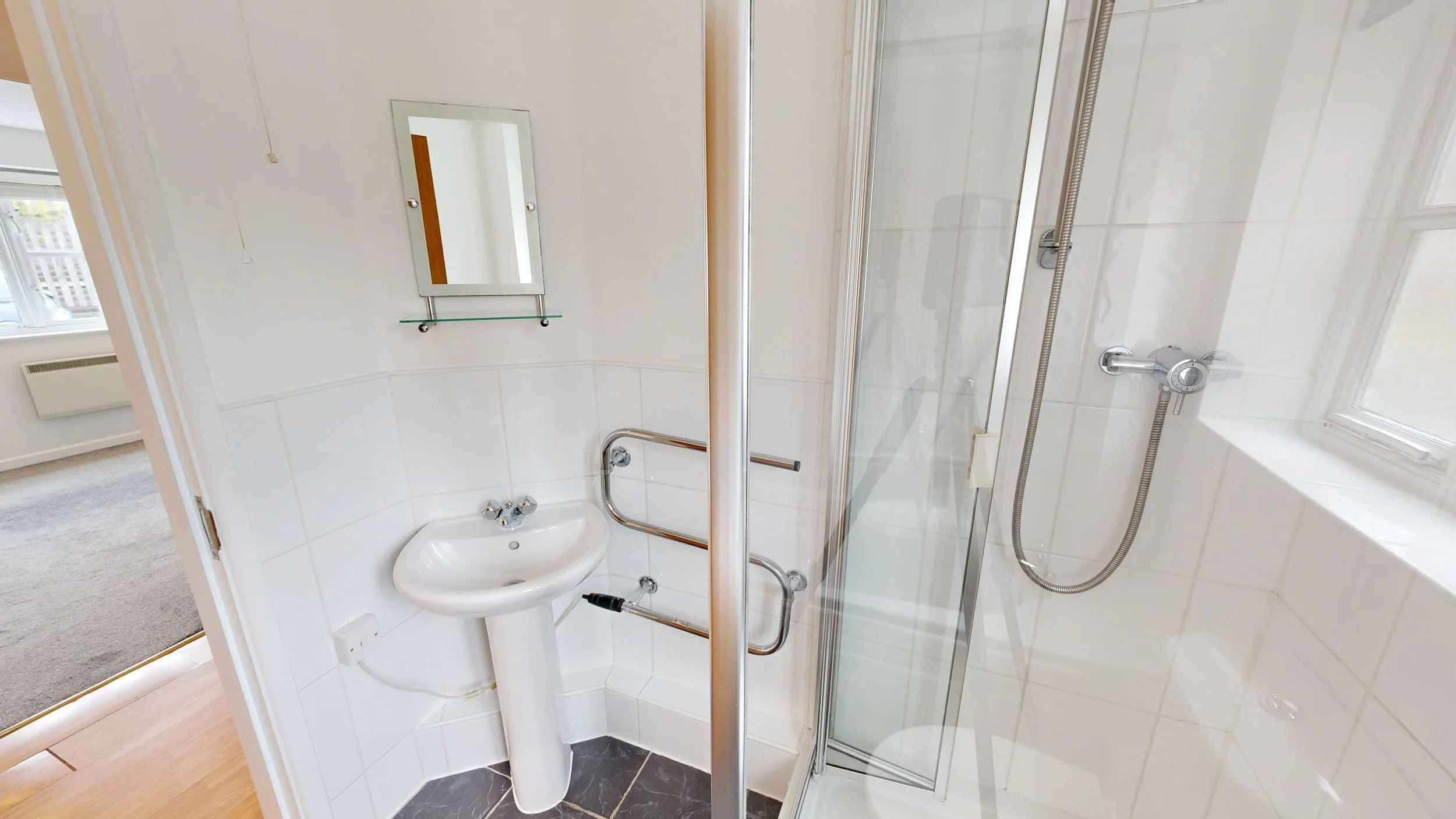 Small bathroom with a corner shower enclosure, a pedestal sink, and a small mirror with a glass shelf above it.