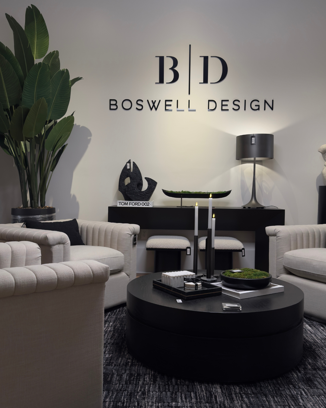 Interior of an office or design studio with modern decor, including white sofas, a round black coffee table, a large potted plant, and wall decor with the sign 'Boswell Design'. Modern furniture and home decor store in New Orleans.
