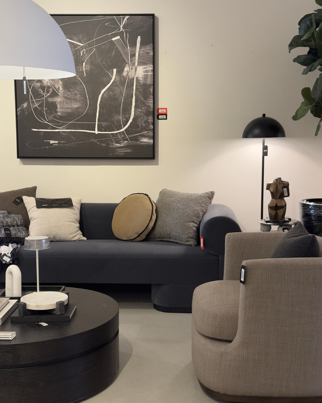 Modern living room with black sofa, textured pillows, round beige chair, abstract black and white painting, black table, and contemporary lamps. Modern furniture and home decor store in New Orleans.
