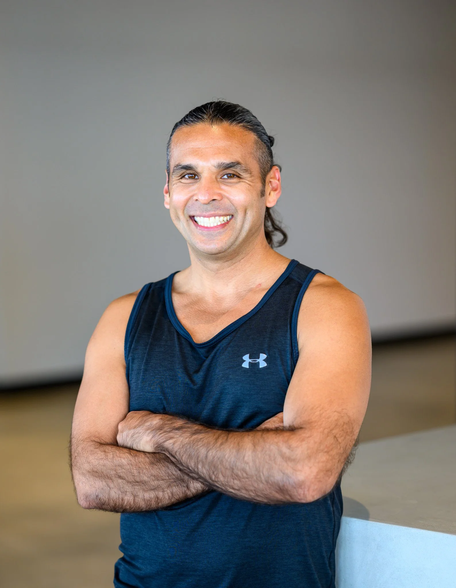 Smiling person with arms crossed wearing a sleeveless athletic shirt, standing indoors.