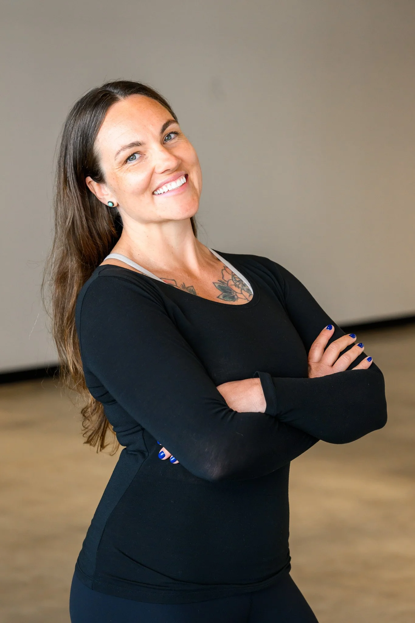 Smiling person in a black top with crossed arms in a neutral setting.