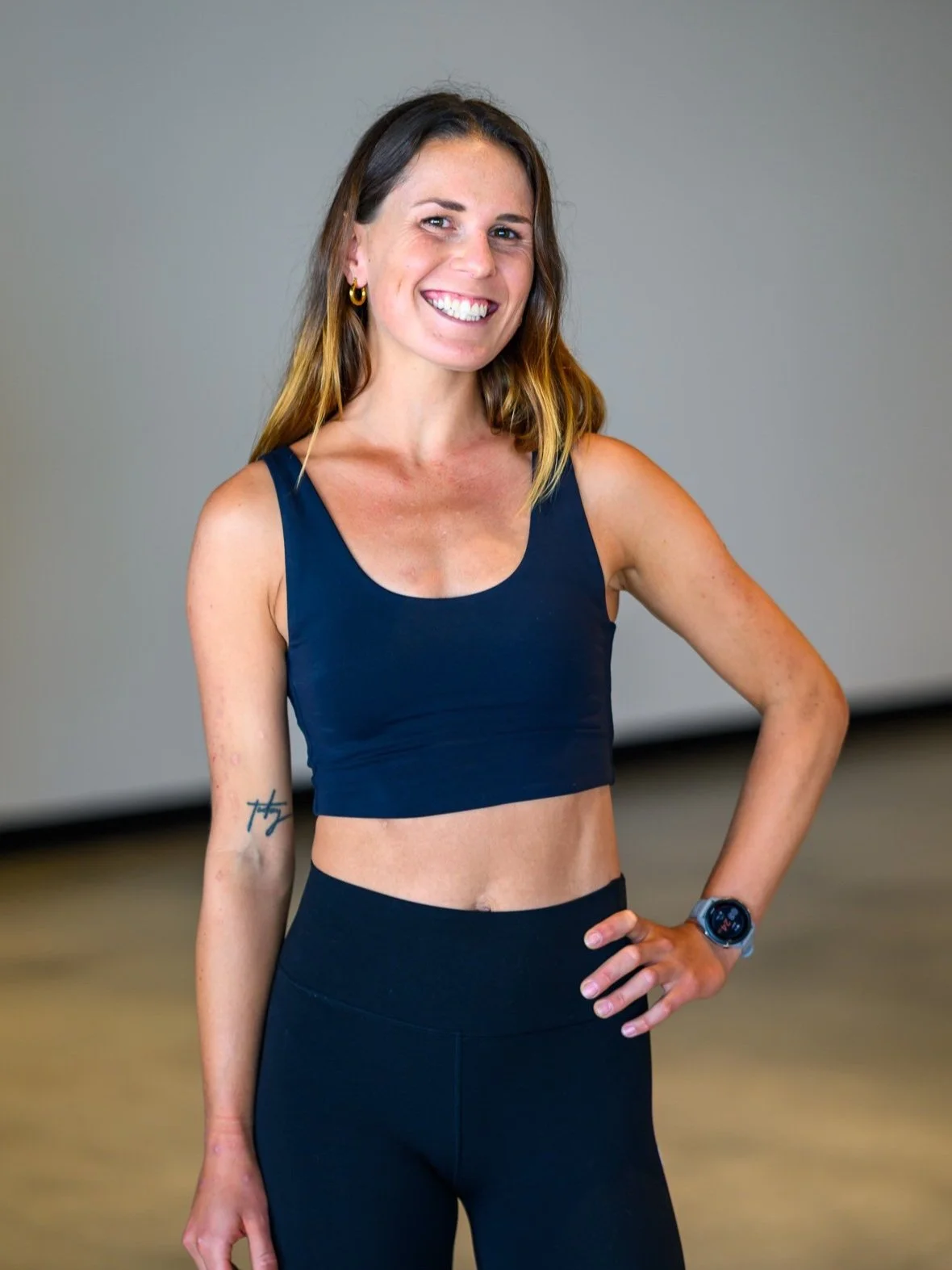 A woman in workout clothing smiling with one hand on her hip.