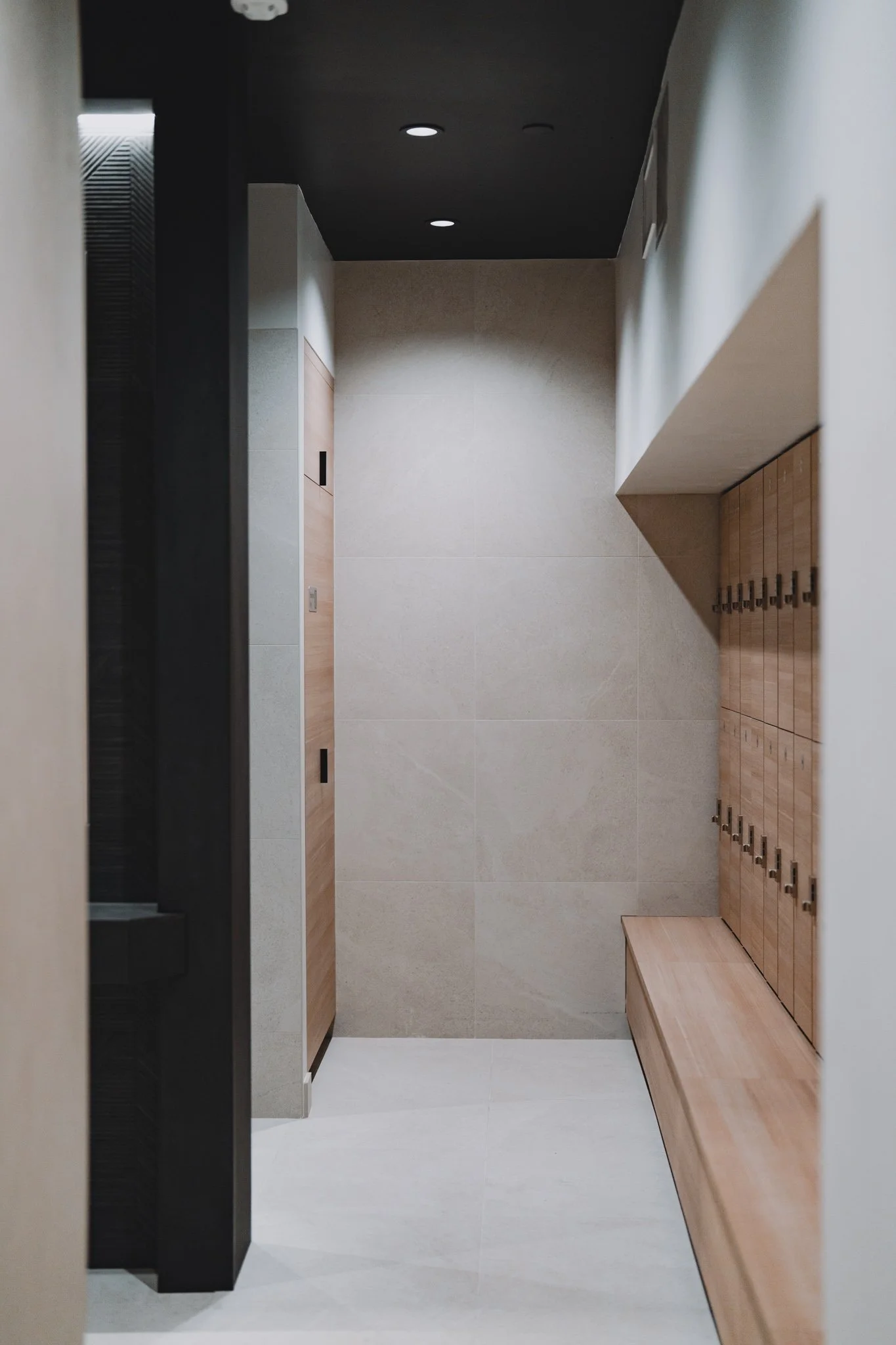 Empty locker room with beige walls, wooden lockers, a small bench, and ceiling lights.