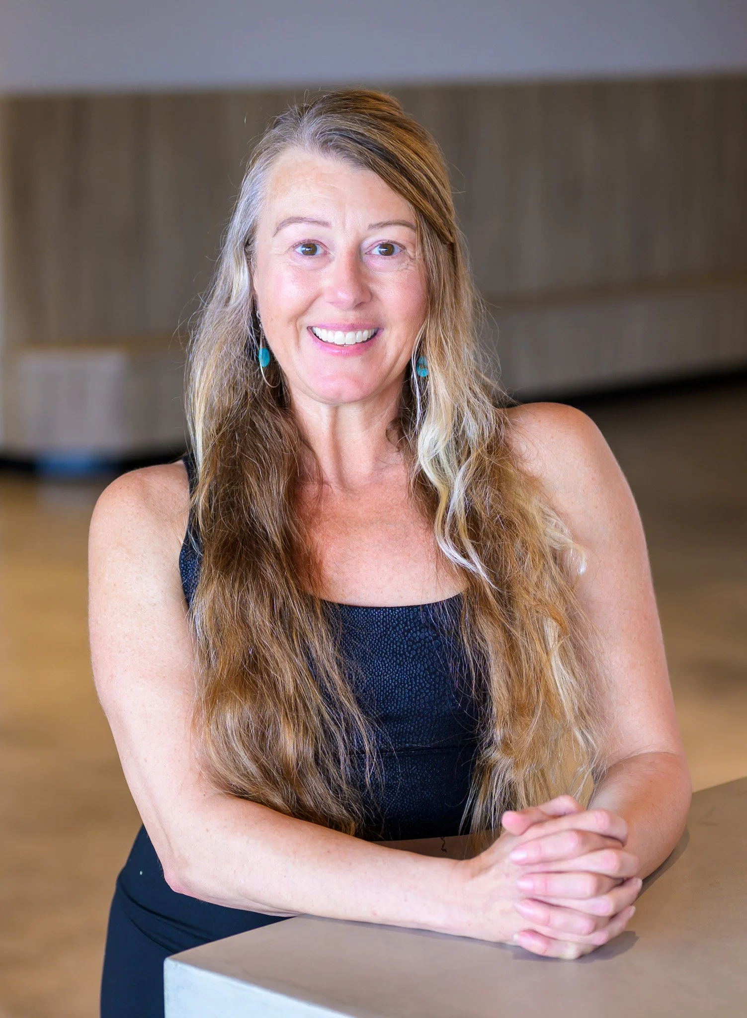 A woman practicing yoga outdoors on a blanket in a grassy field, standing on one leg in a tree pose with hands pressed together above her head, smiling and looking upward.