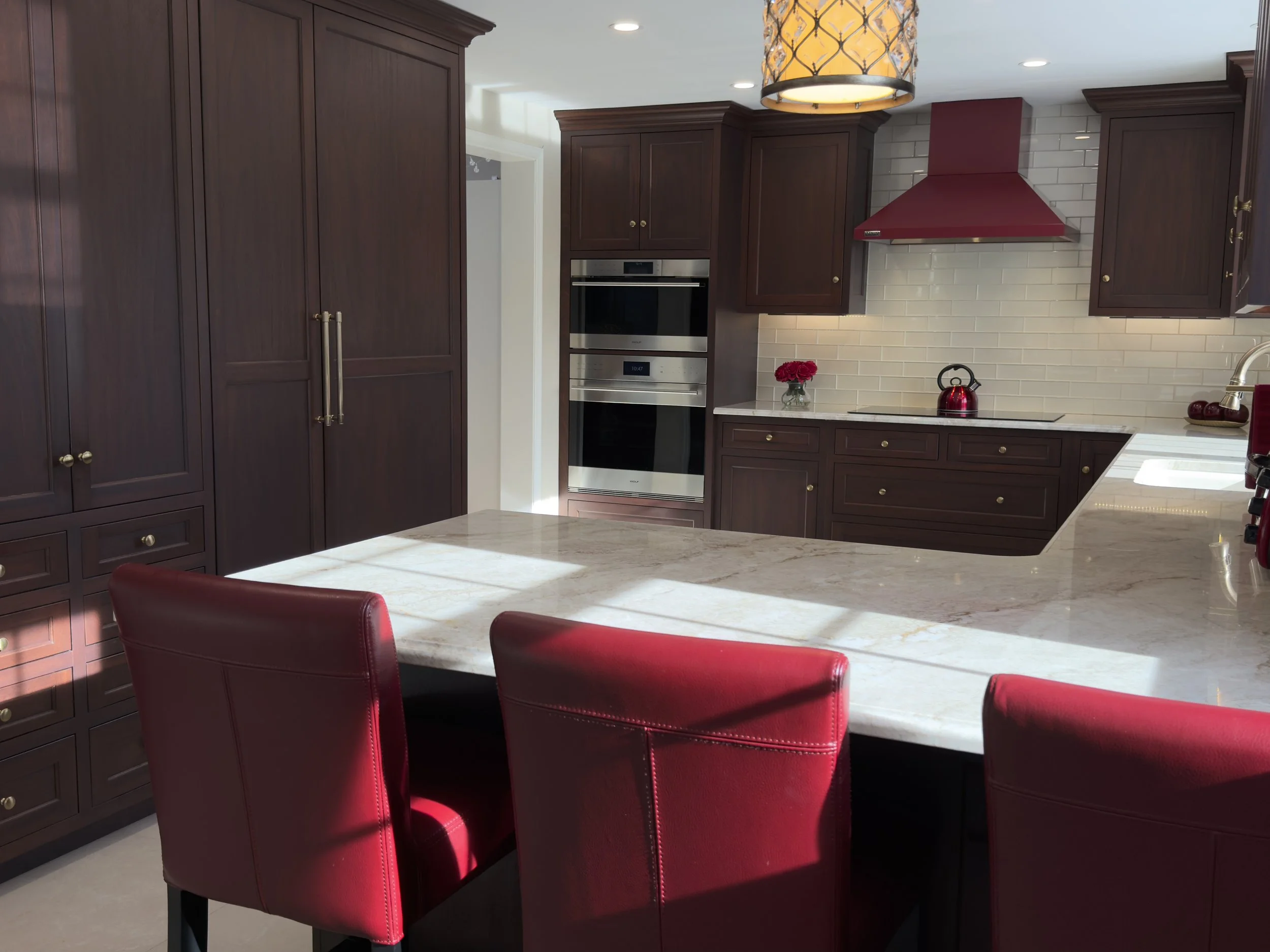 Modern kitchen with mahogany cabinets,  stainless steel appliances, marble countertops, hardwood floors, warm pendant lights