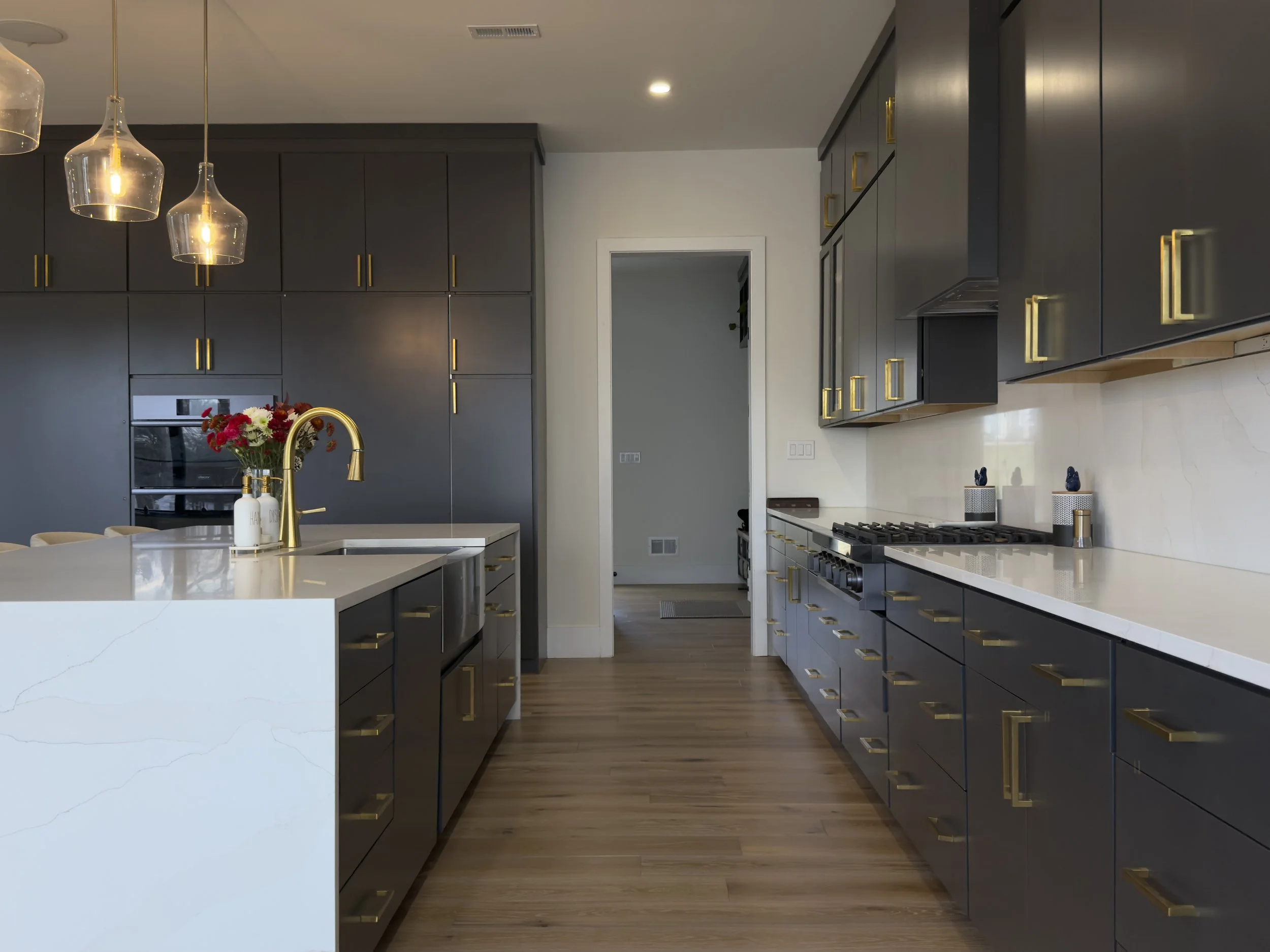 Modern kitchen with black cabinets, appliances, marble countertops, hardwood floors, warm pendant lights