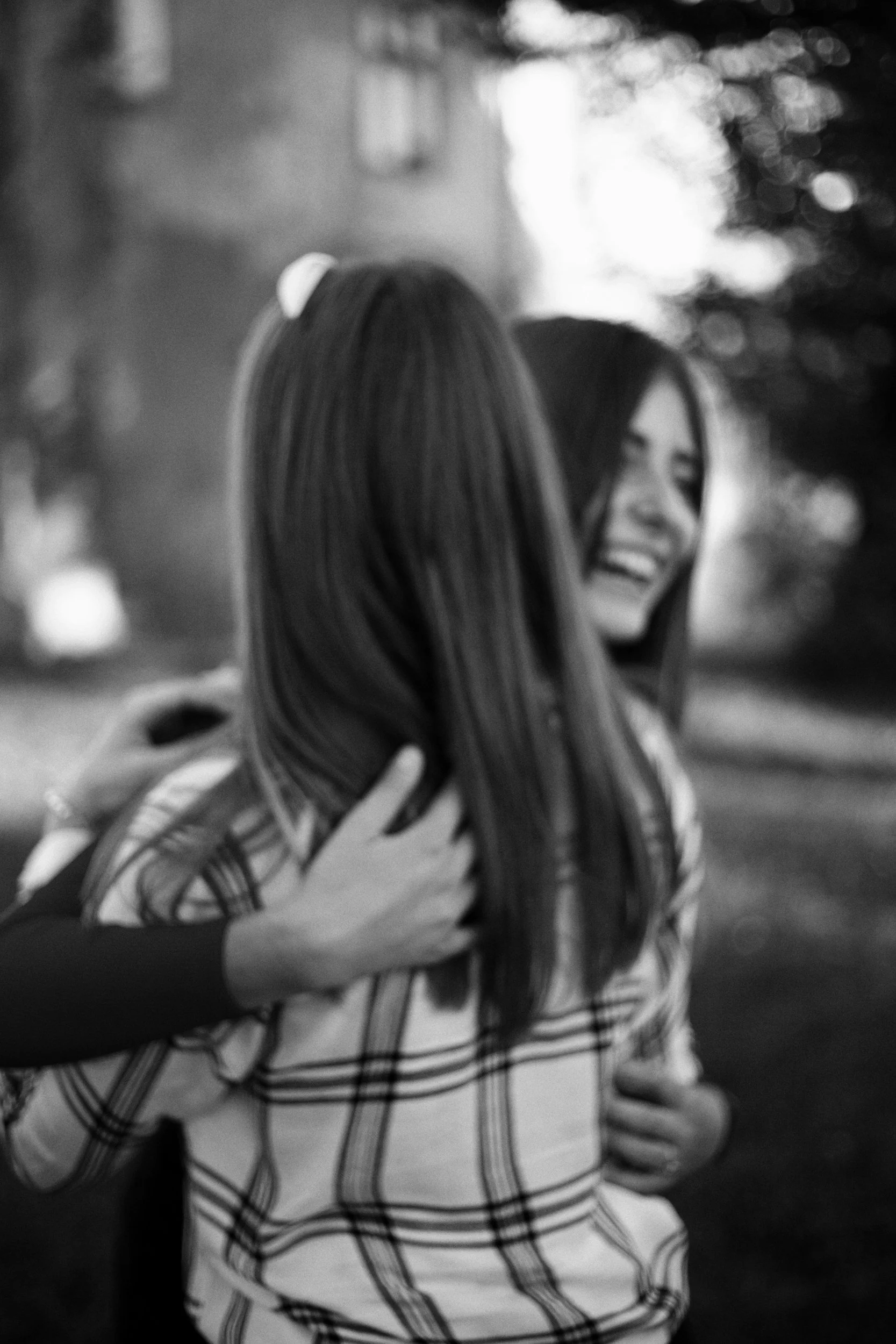 Two women hugging outdoors, one smiling, in black and white.