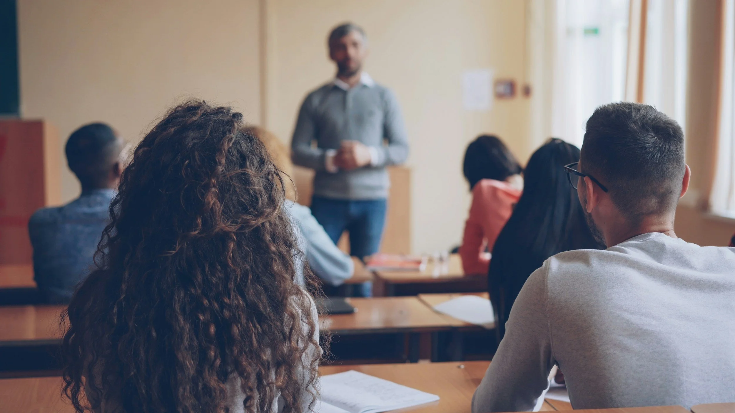 A classroom with students sitting at desks and a teacher standing at the front.