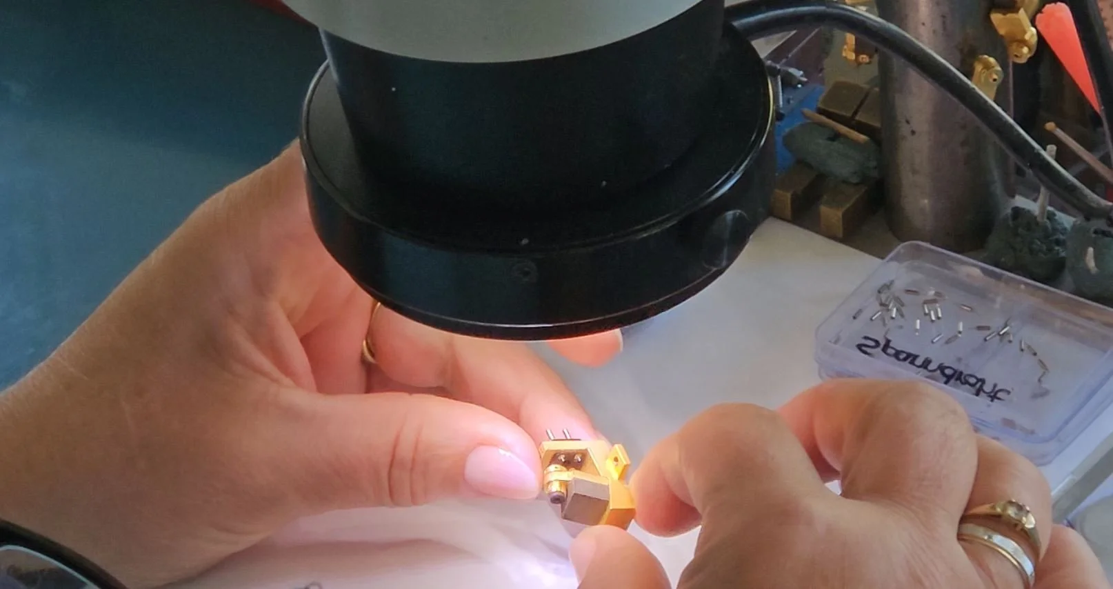 Closeup of a technicians hands and a gold Benz cartridge body under a microscope during assembly.