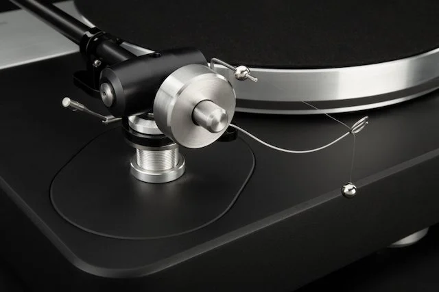 Detail of Dr. Feickert Analogue Volare turntable in black finish, highlighting tonearm pivot assembly, and machined aluminum platter edge.