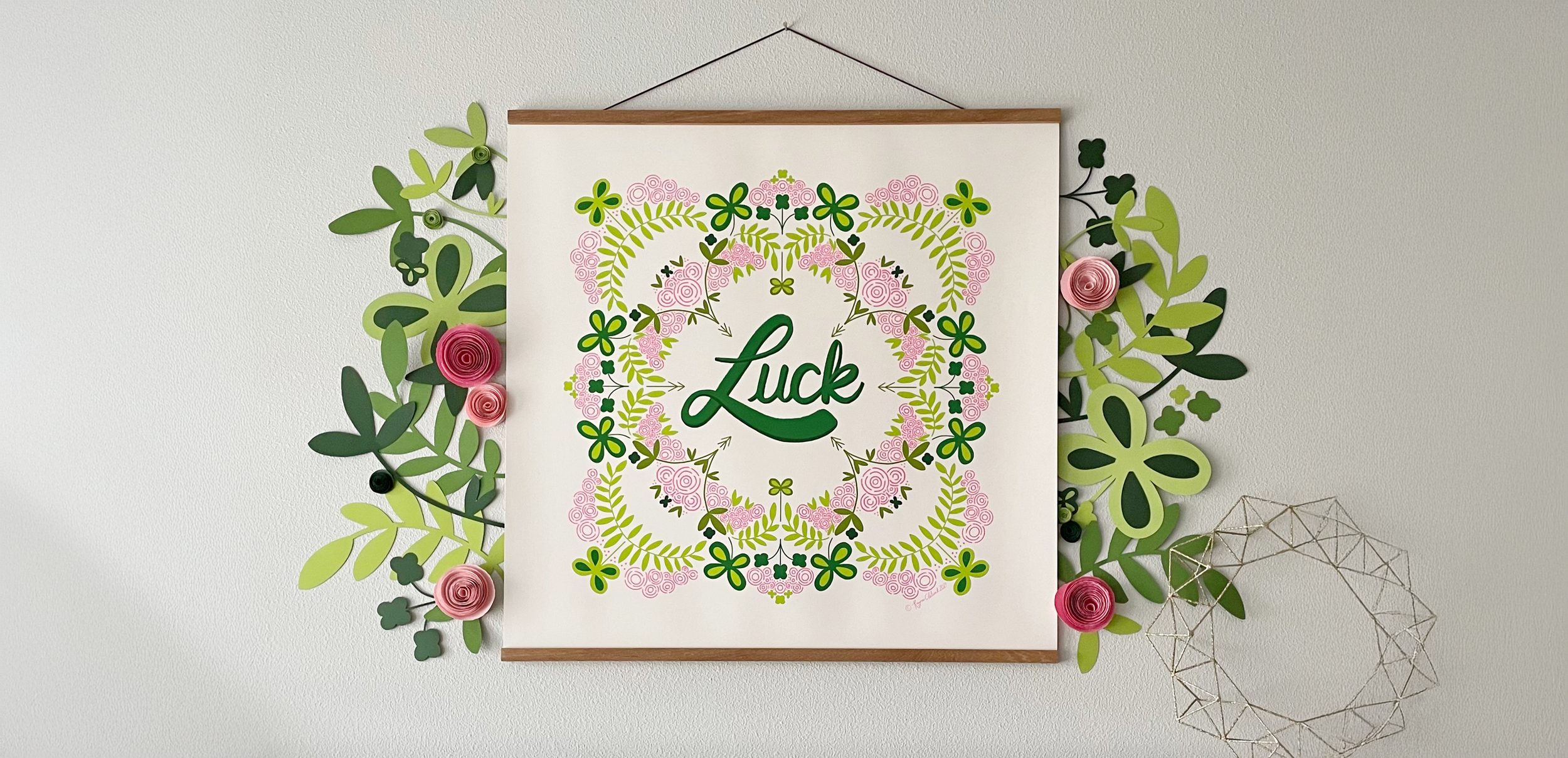 Large wall hanging of symmetrical illustration with abstract roses and four leaf clovers in pinks and greens with the hand lettered word Luck in the middle.